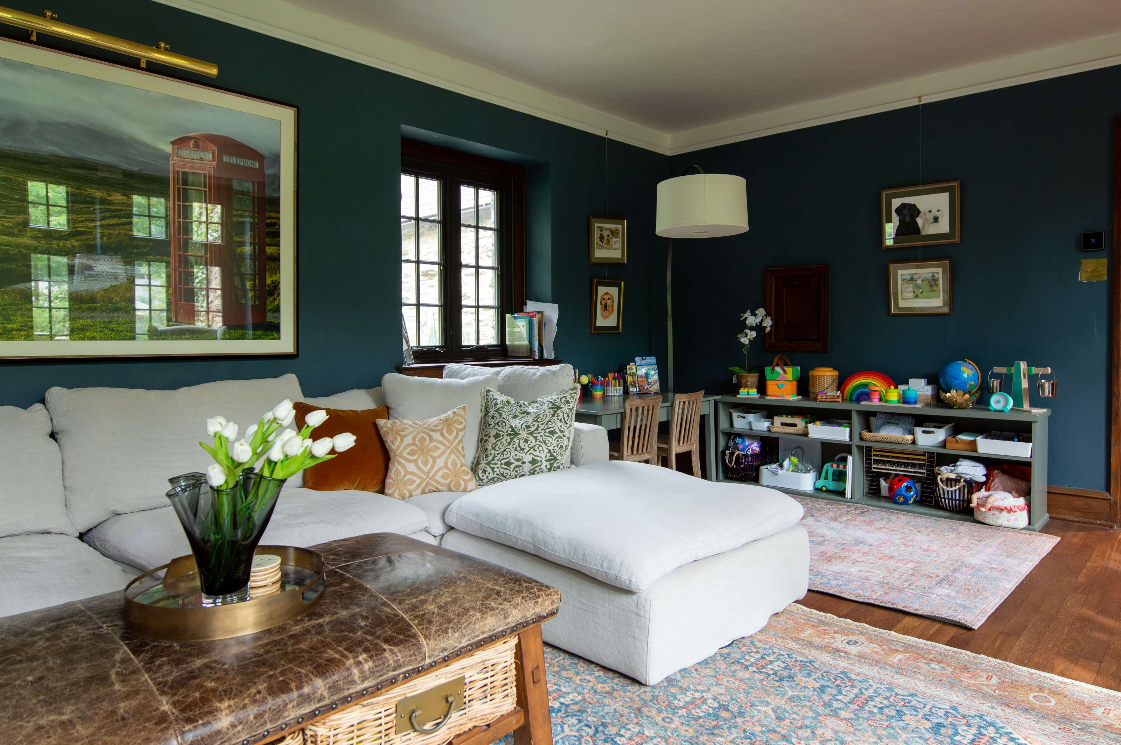 A cozy living room features a large sofa, a coffee table, and shelves filled with children's toys against a dark green wall.