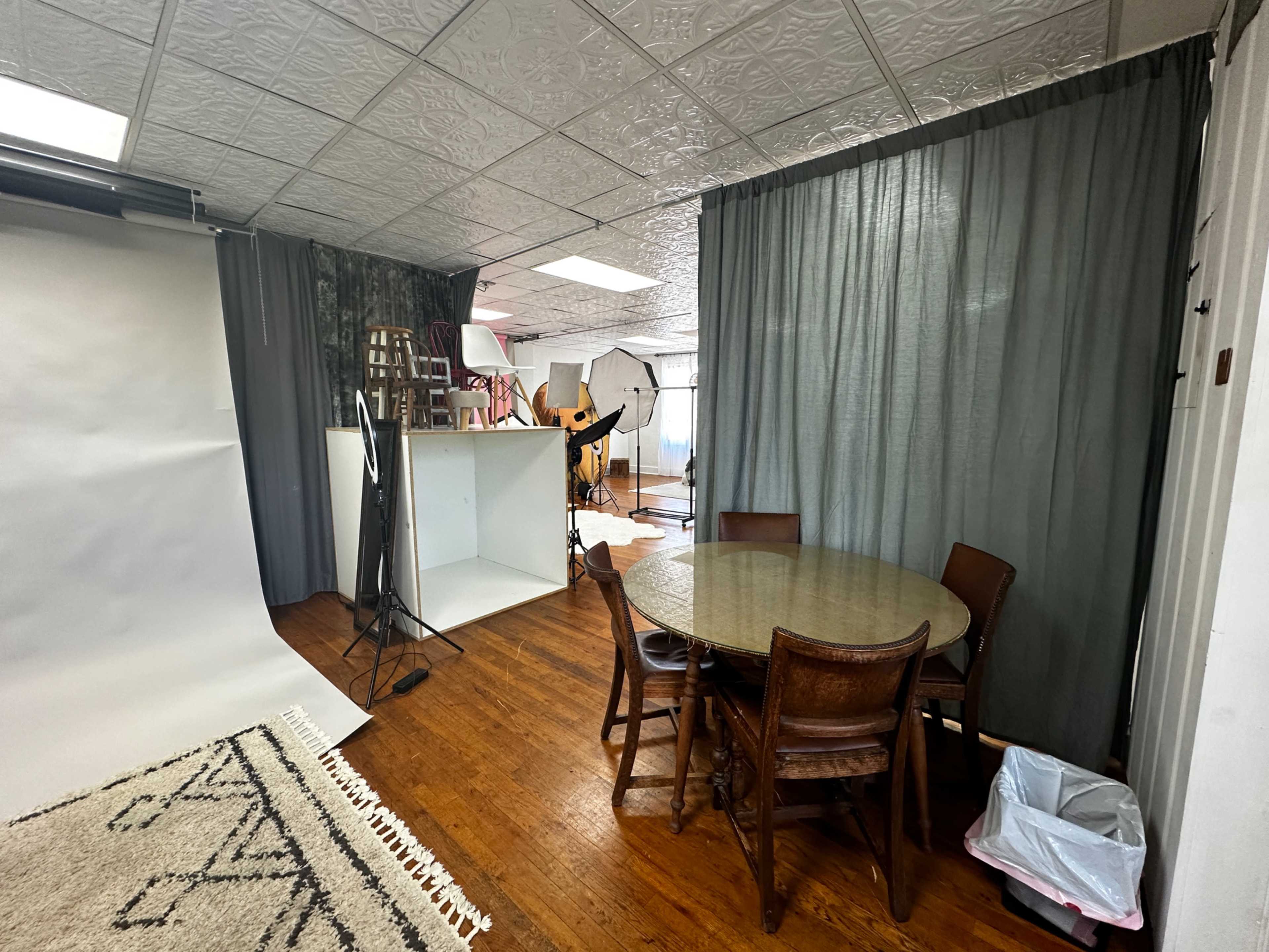 A spacious room containing a circular table with chairs, a white backdrop, and photography equipment set up in the background.