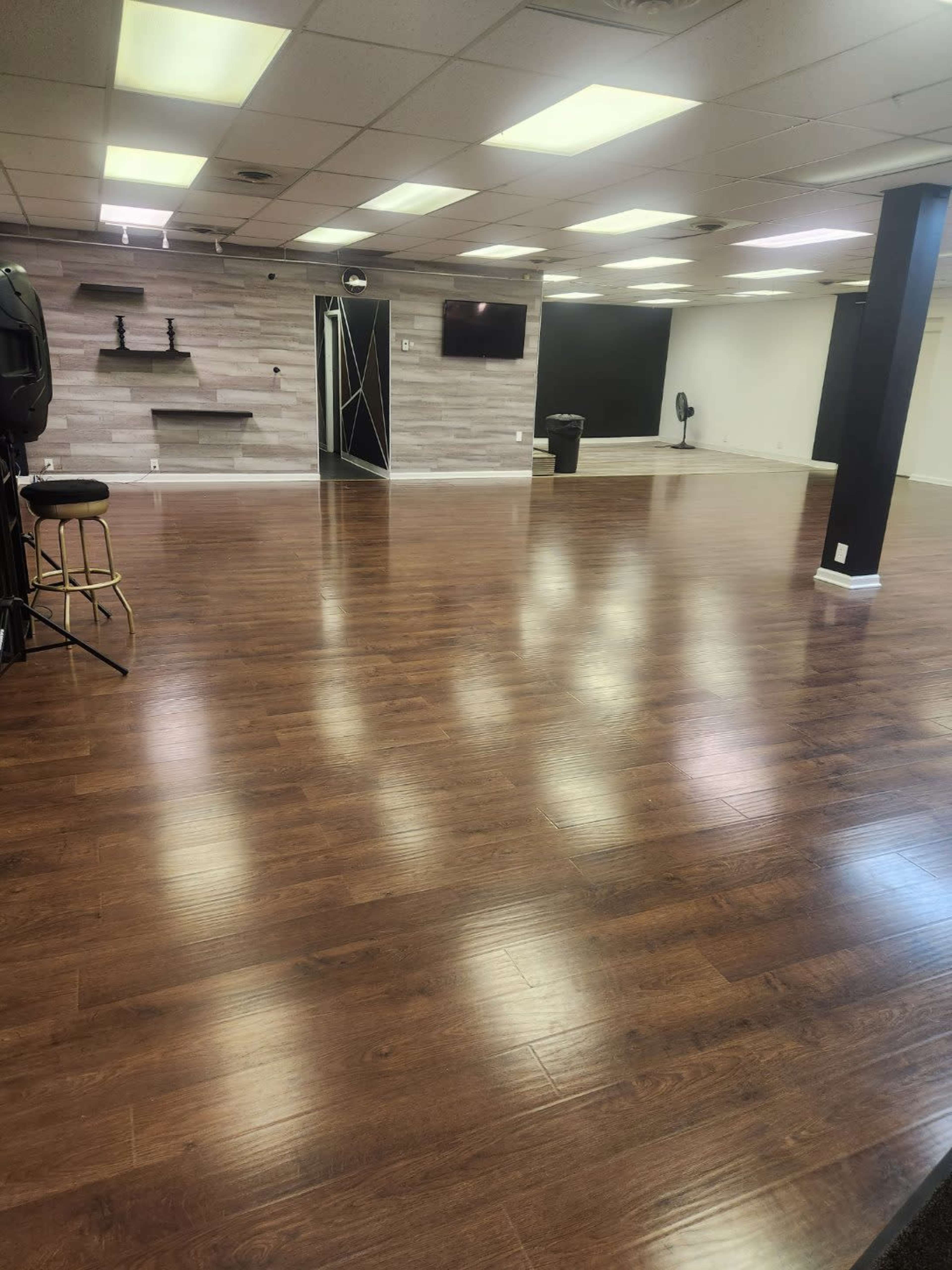 An empty room with polished wooden floors, bright overhead lights, and a gray feature wall with a television and minimalist decor.