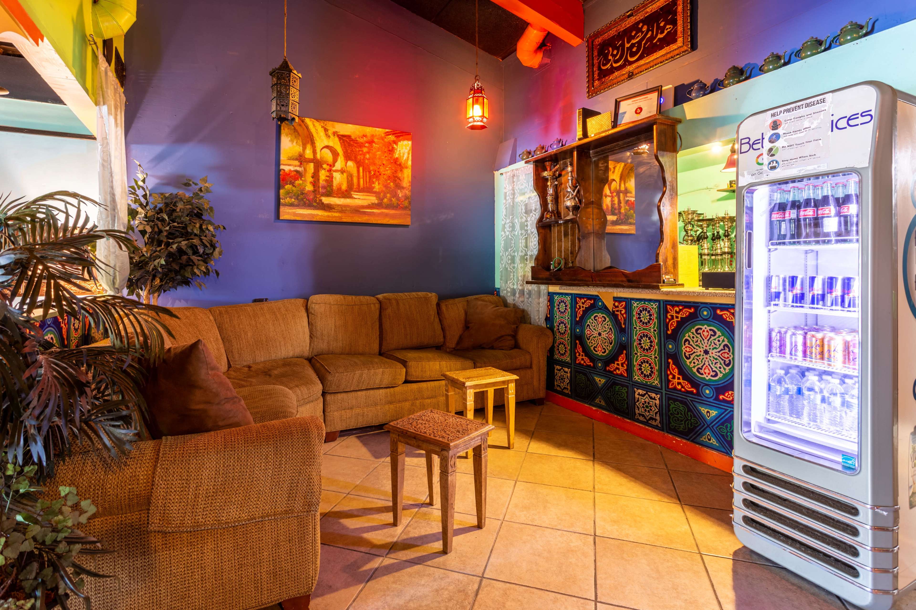 A cozy seating area features a brown couch and wooden table near a brightly colored bar adorned with decorative items and a beverage refrigerator.