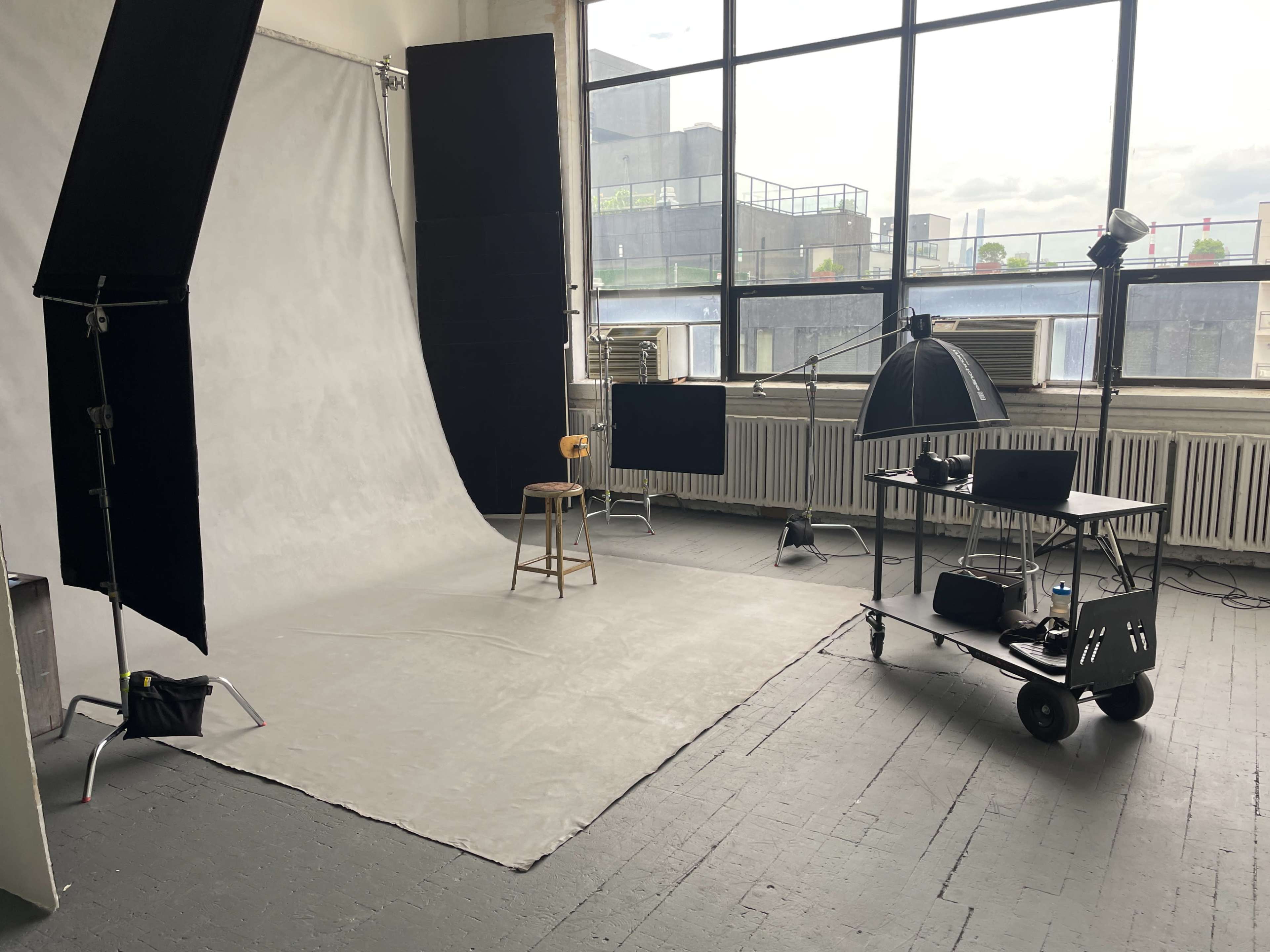 A photography studio with a backdrop, a wooden stool, lighting equipment, and a cart with additional gear.