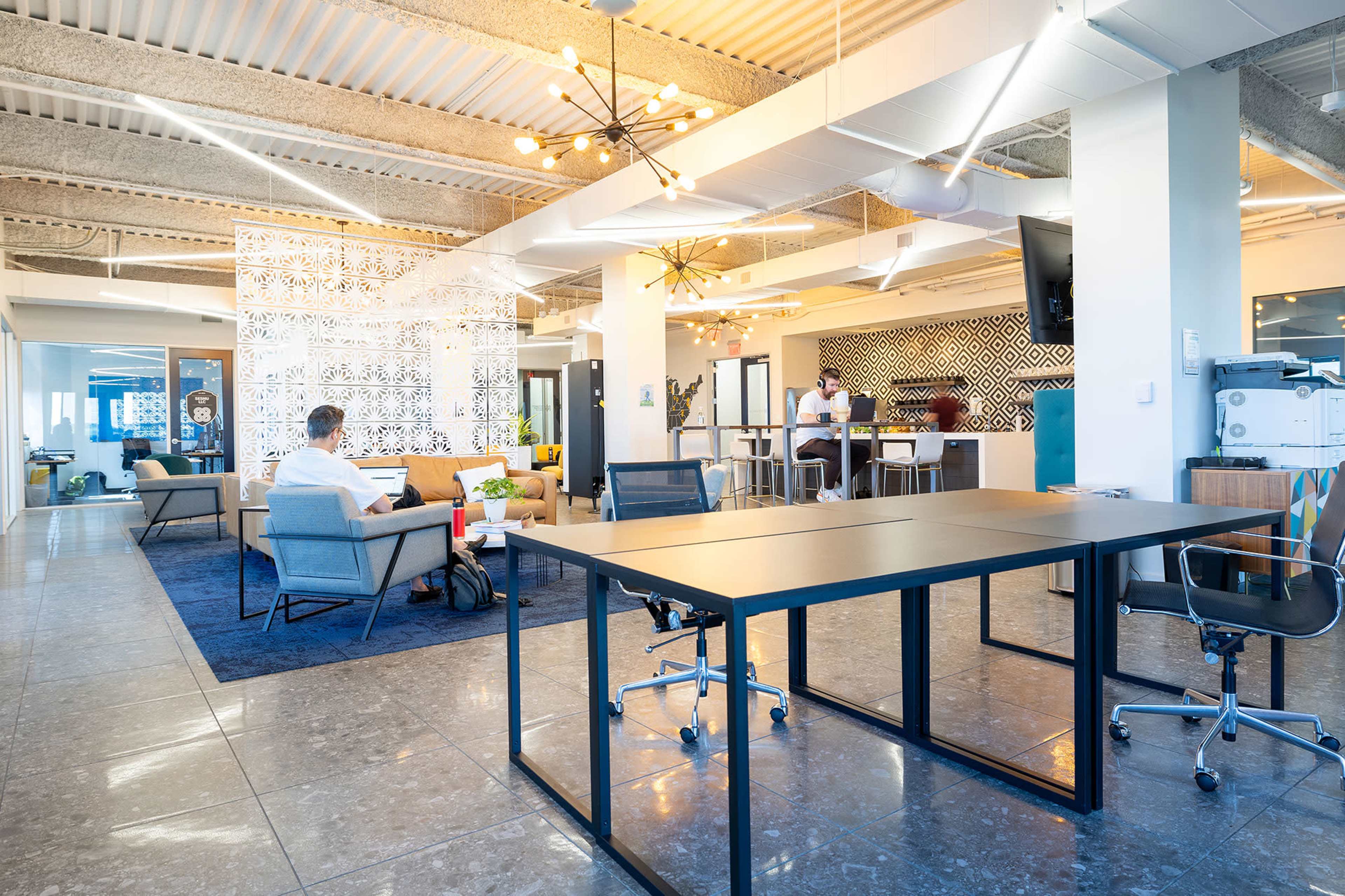 The image shows a modern open office space with a mix of seating areas, workstations, and collaborative spaces.