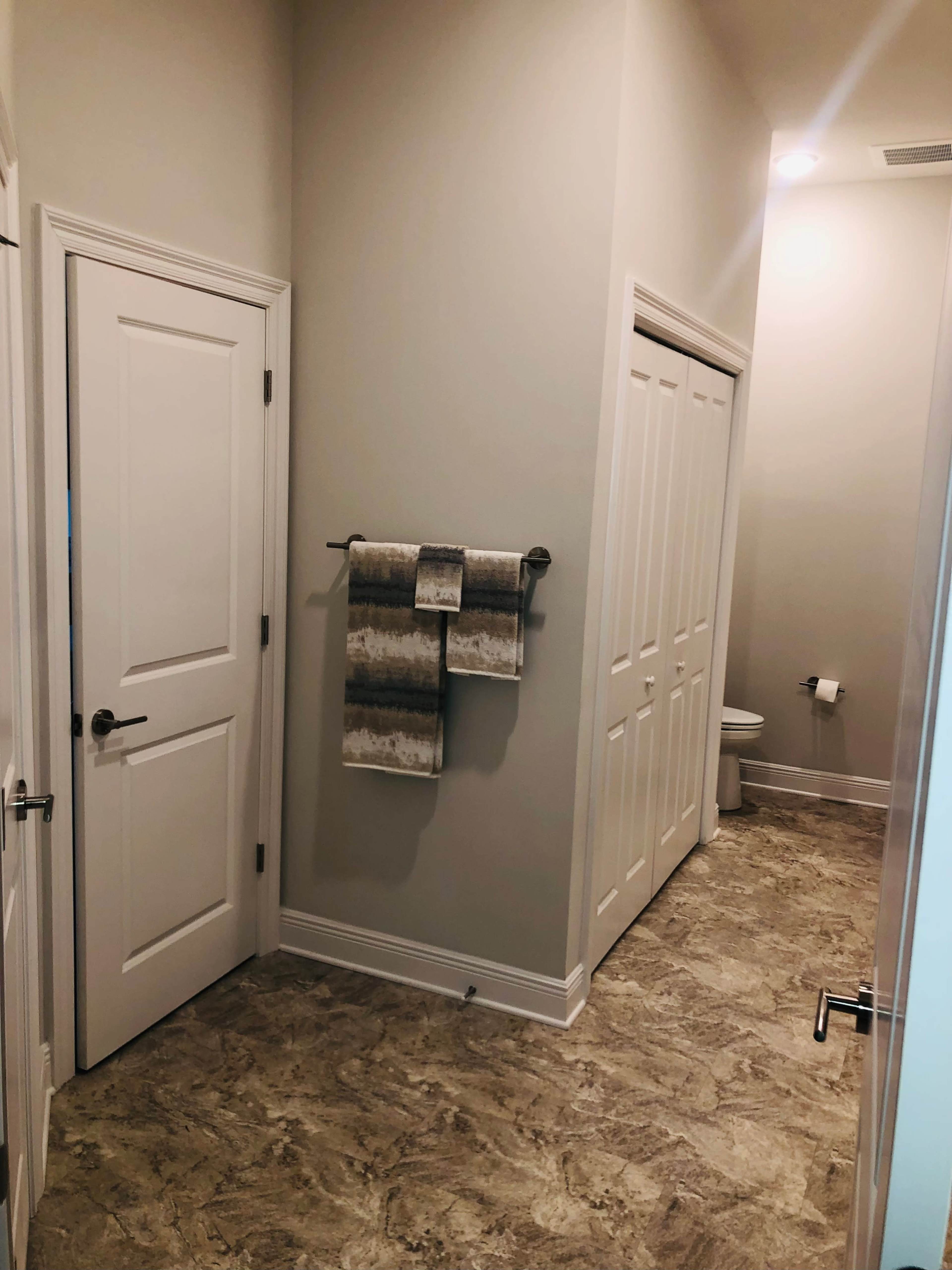 The image shows a well-lit hallway leading to a bathroom with a towel rack and a closed closet door.