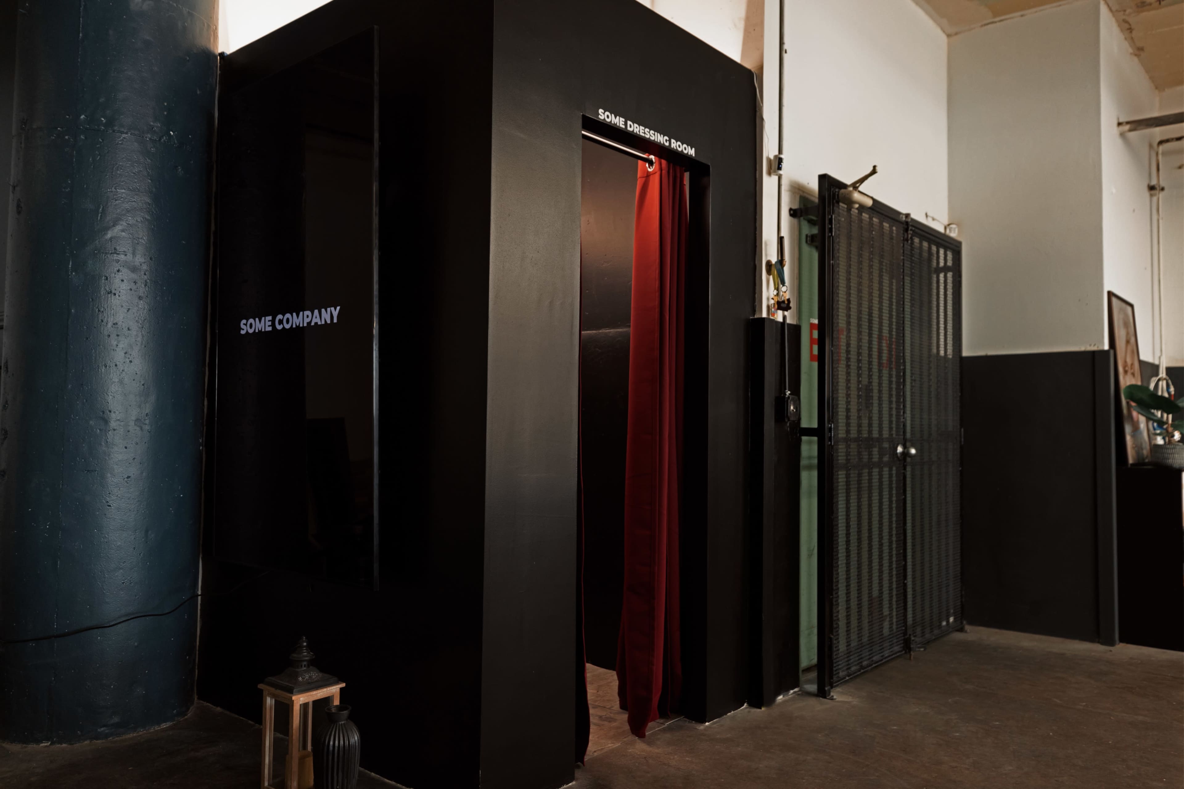 The image shows a dark, enclosed space with a red curtain entrance labeled "SOME COMPANY" adjacent to a metal gate in a warehouse-like setting.