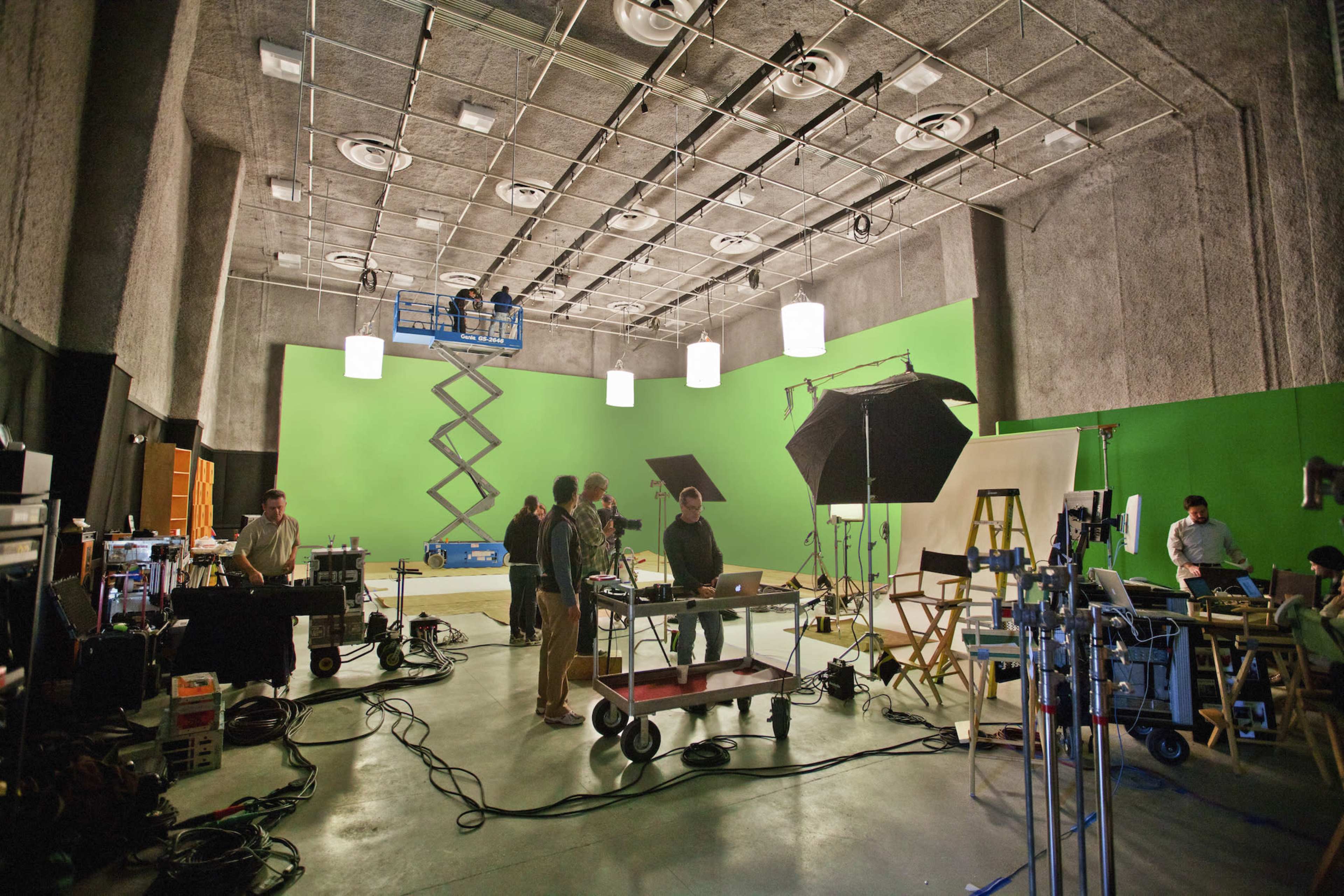 A film studio equipped with a green screen, lighting equipment, and a group of people preparing for a shoot.