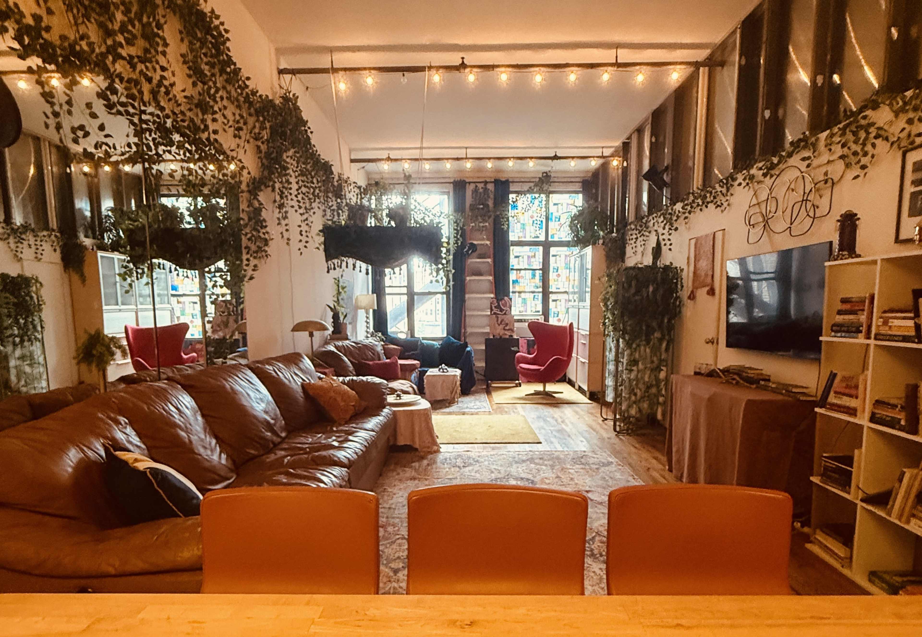 The image depicts a cozy living room with a large brown leather sofa, decorative plants, and a warm ambiance created by string lights.