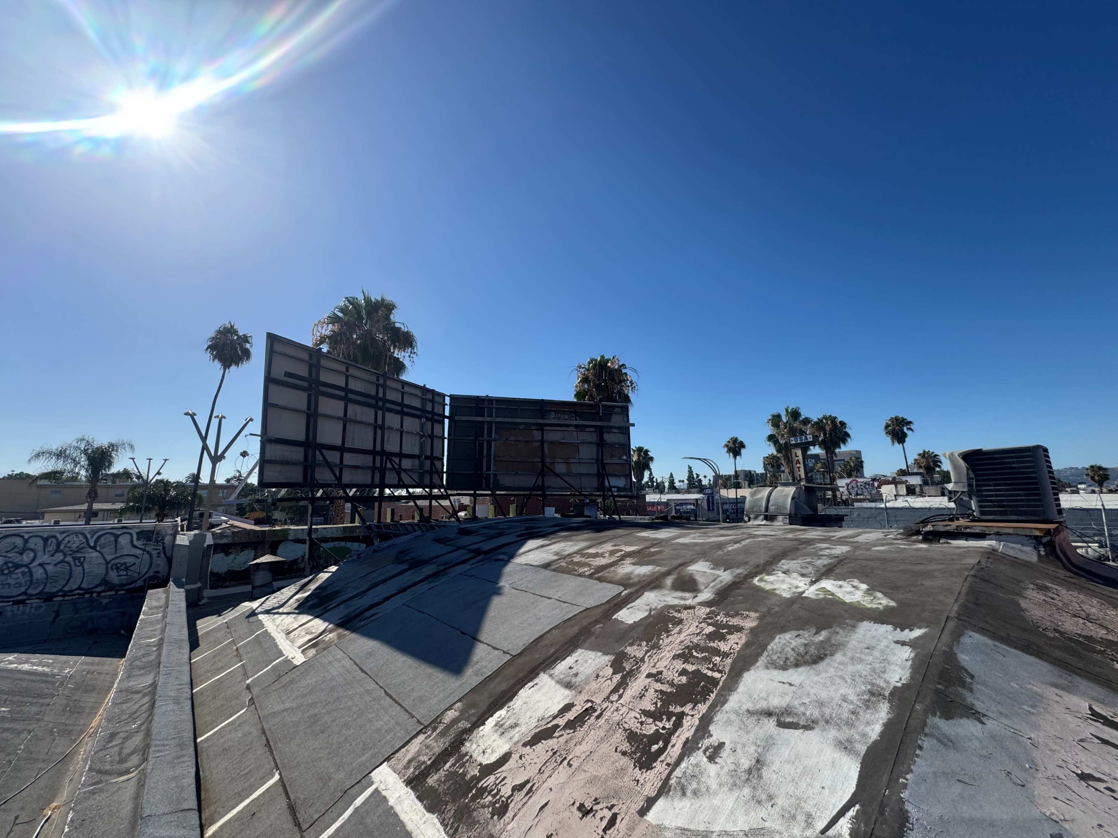 A rooftop scene features a dilapidated billboard structure surrounded by palm trees under a clear blue sky.