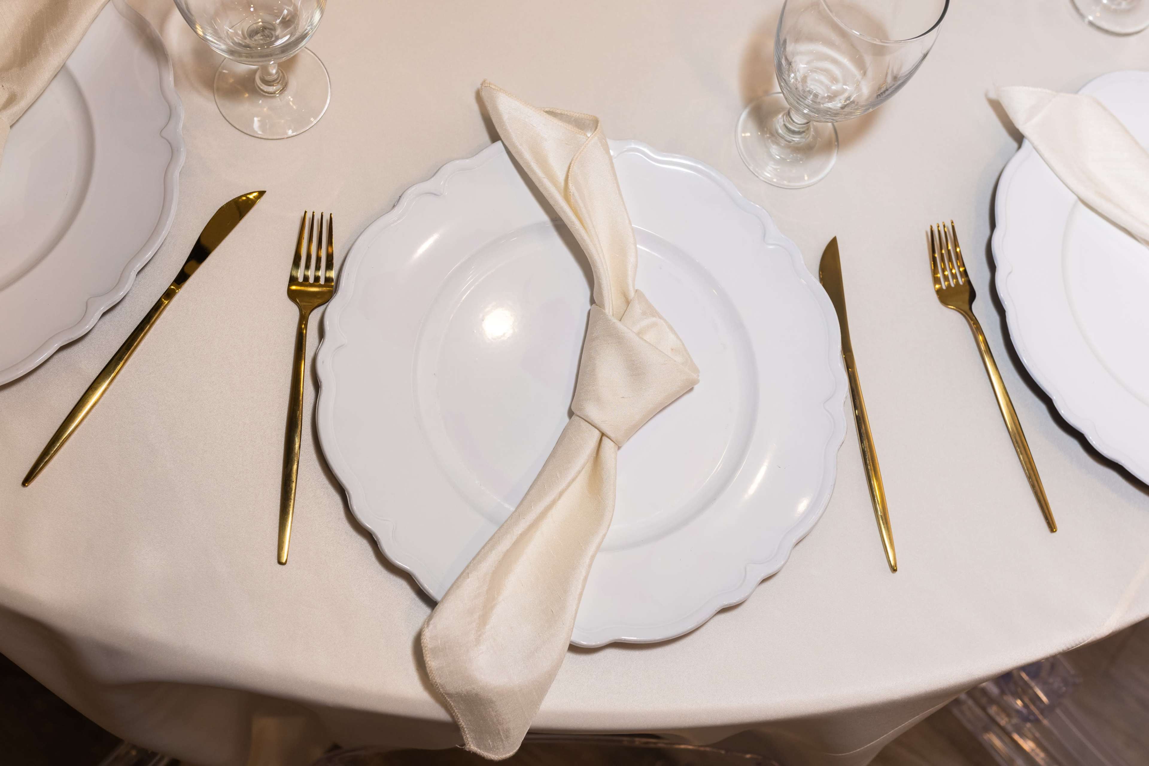The image shows a neatly set dining table with white plates, golden cutlery, and folded cream napkins.