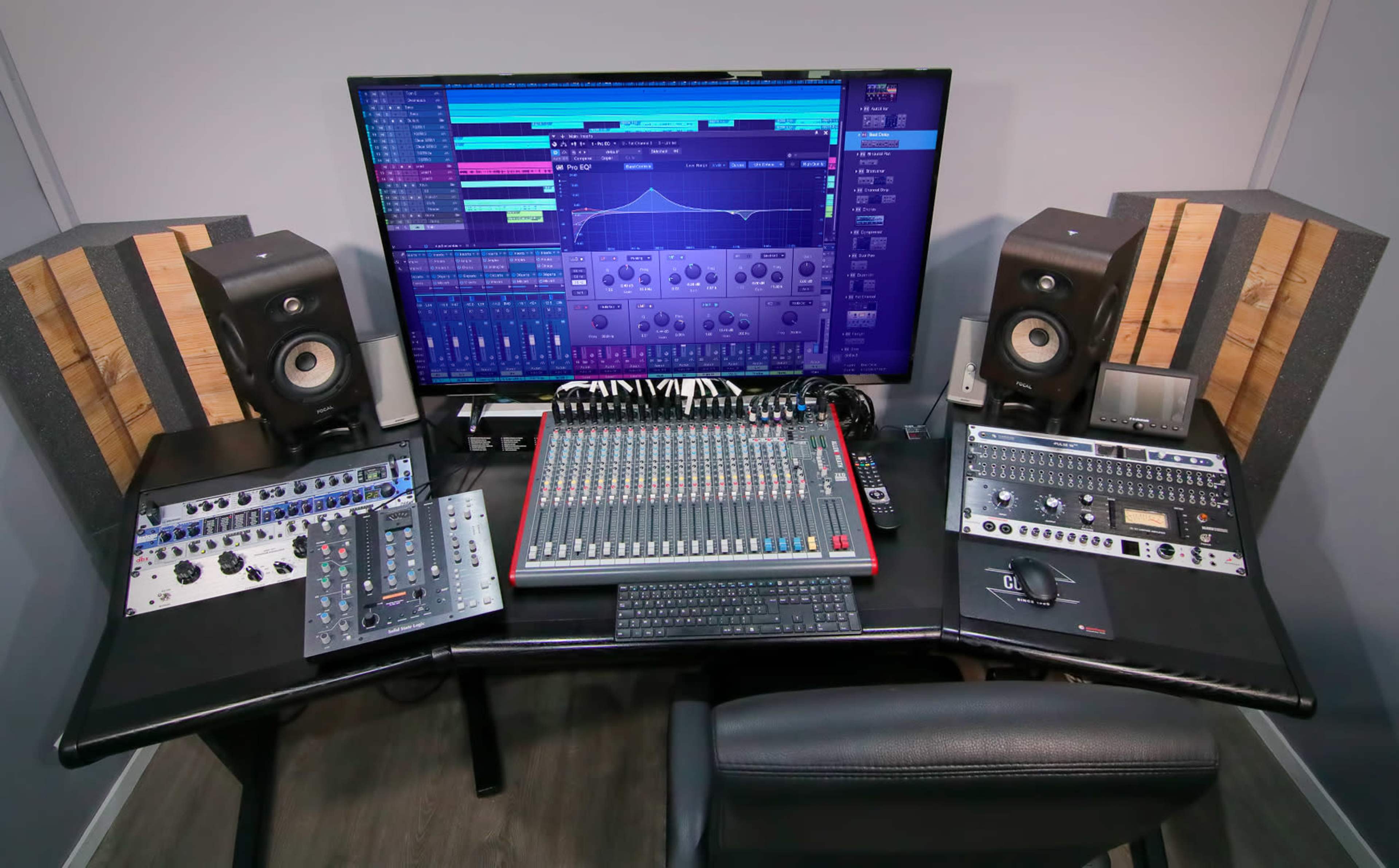 A modern audio mixing studio setup with a large monitor displaying sound editing software, a mixing console in the center, and various audio equipment on a sleek desk.
