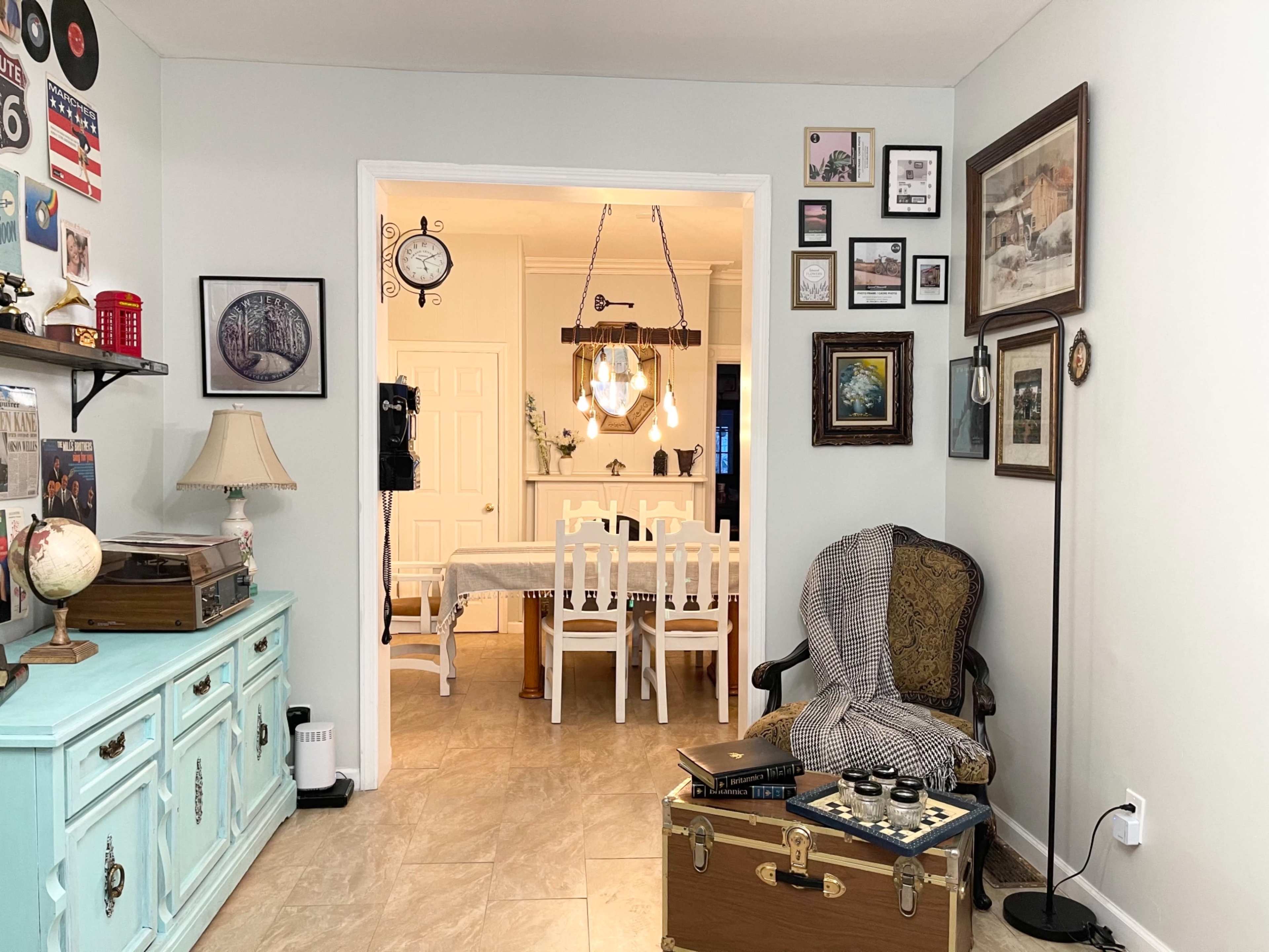 A cozy, decorated living space features a sitting area with a chair and trunk, leading to a dining area furnished with a table and chairs.