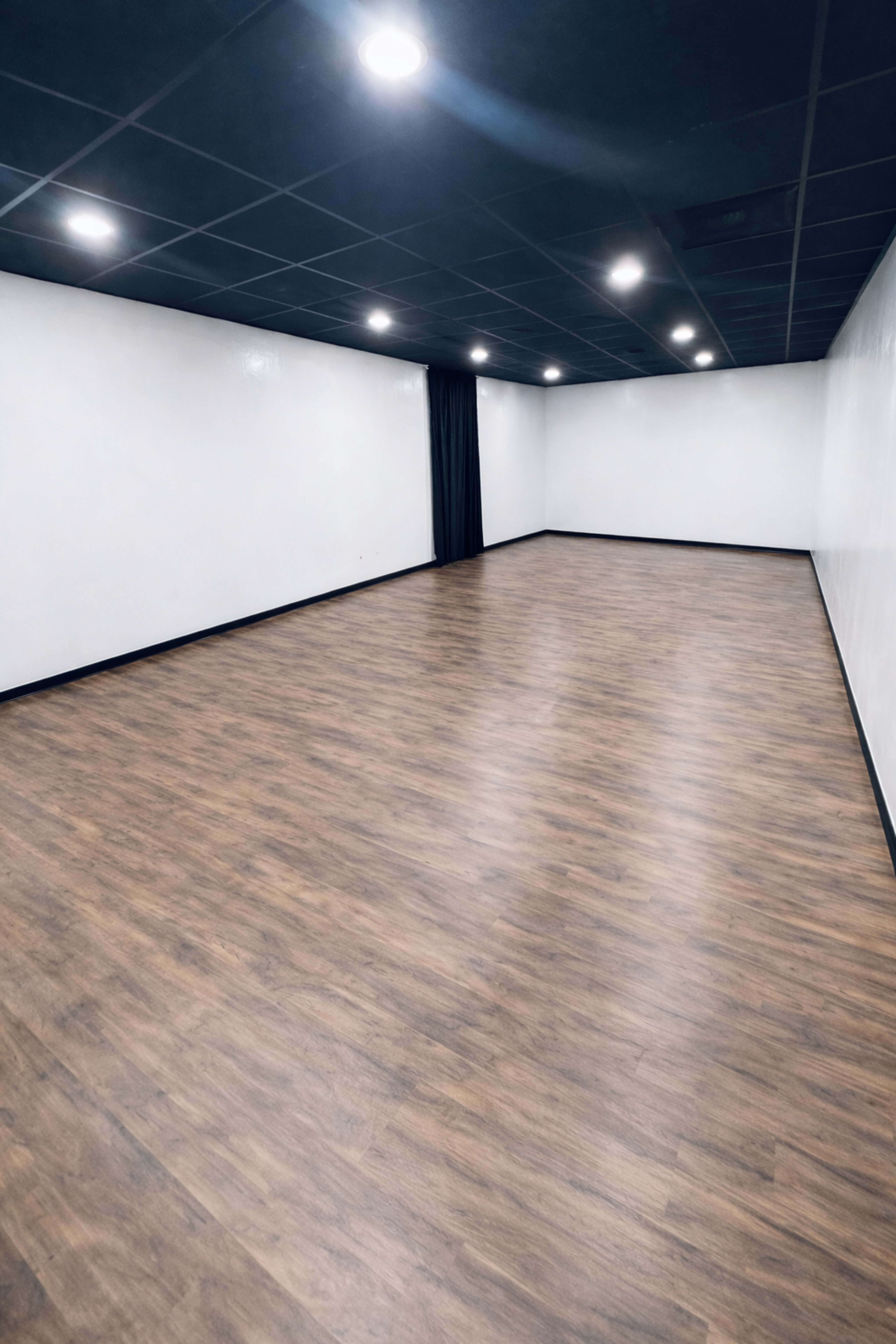 The image shows an empty room with a wooden floor, white walls, and ceiling lights.