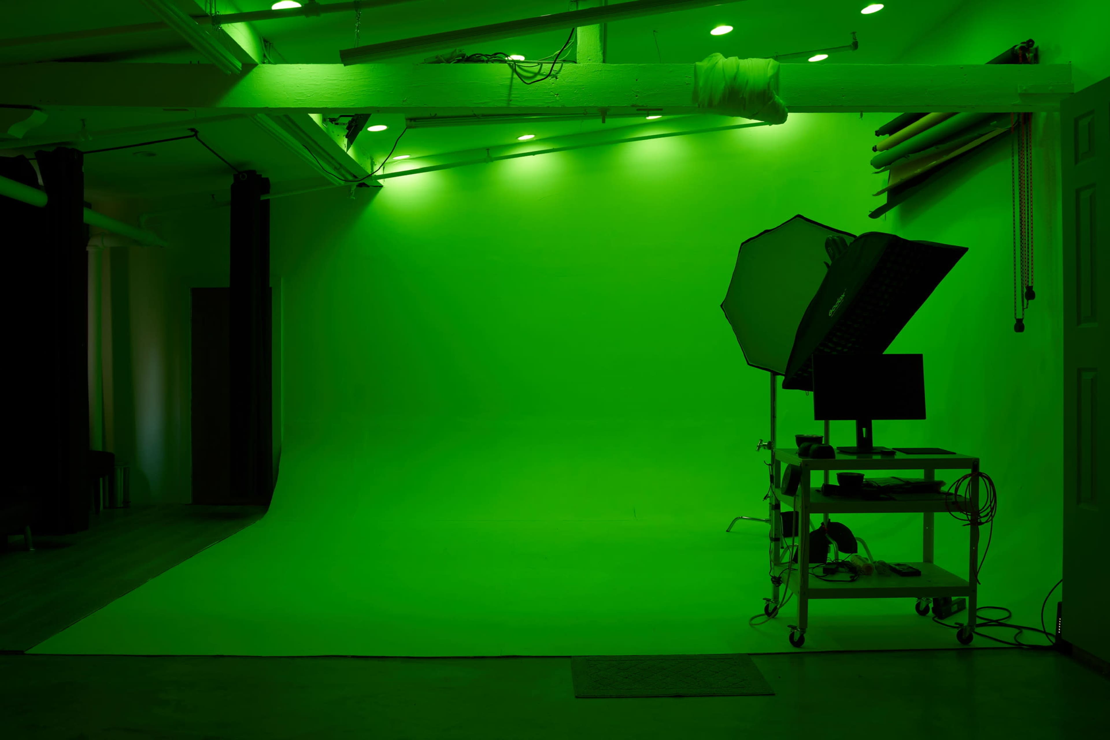 A photography studio features a green backdrop and lighting setup on one side, with an equipment cart nearby.