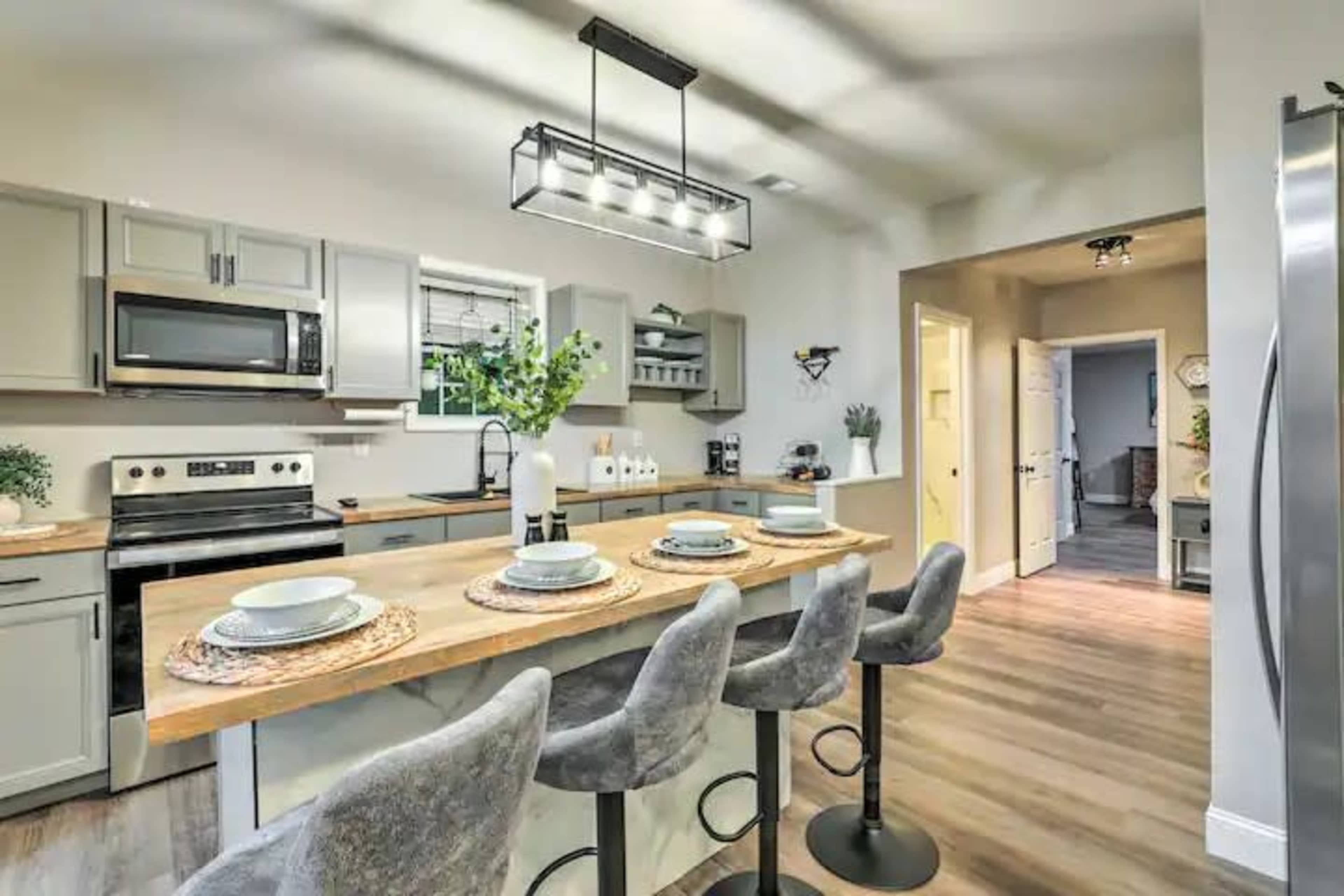 A modern kitchen with a central island featuring bar stools, stainless steel appliances, and light gray cabinetry.