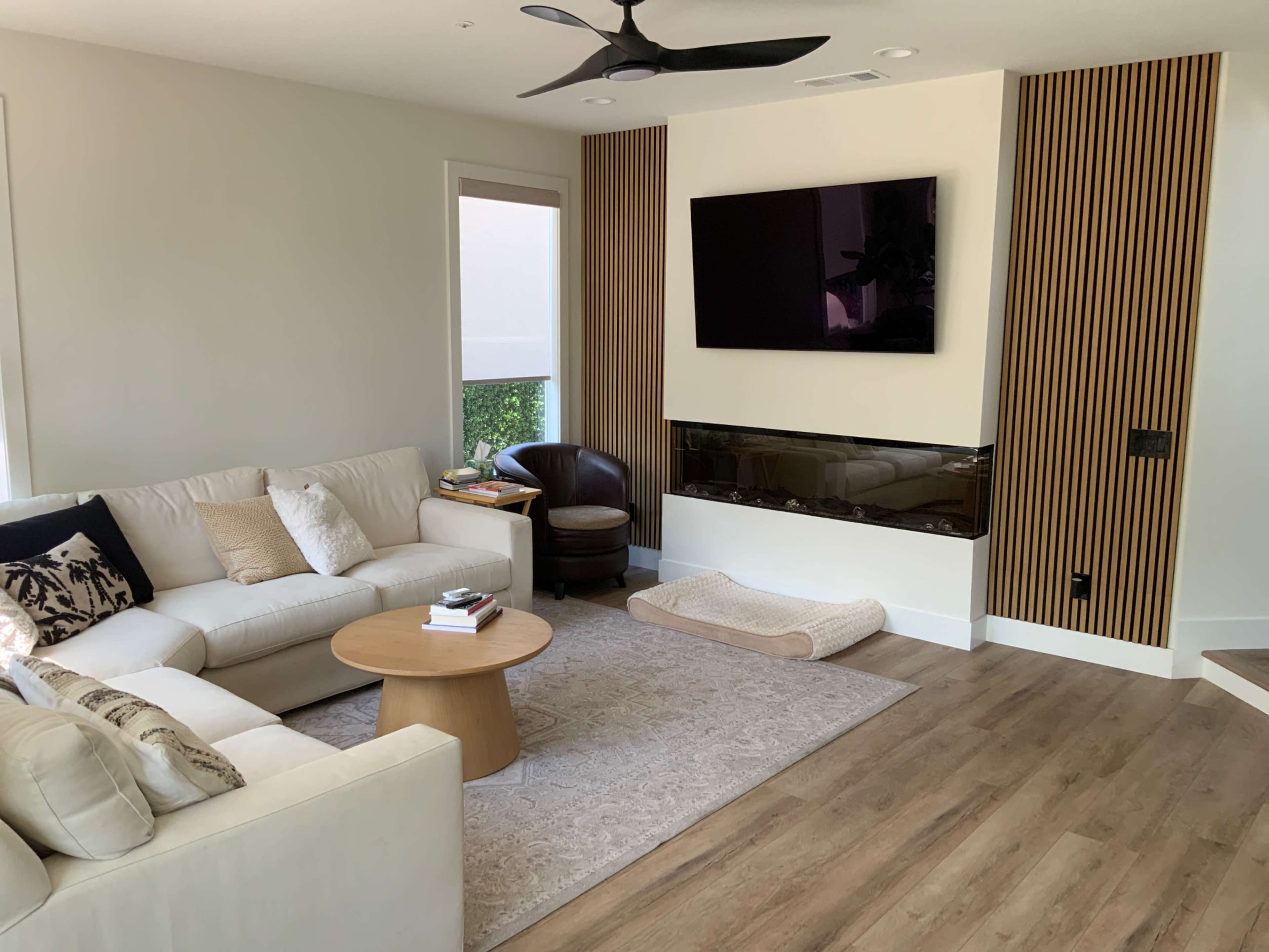 A modern living room features a white sectional sofa, a coffee table, a mounted TV, and a decorative fireplace and wall paneling.