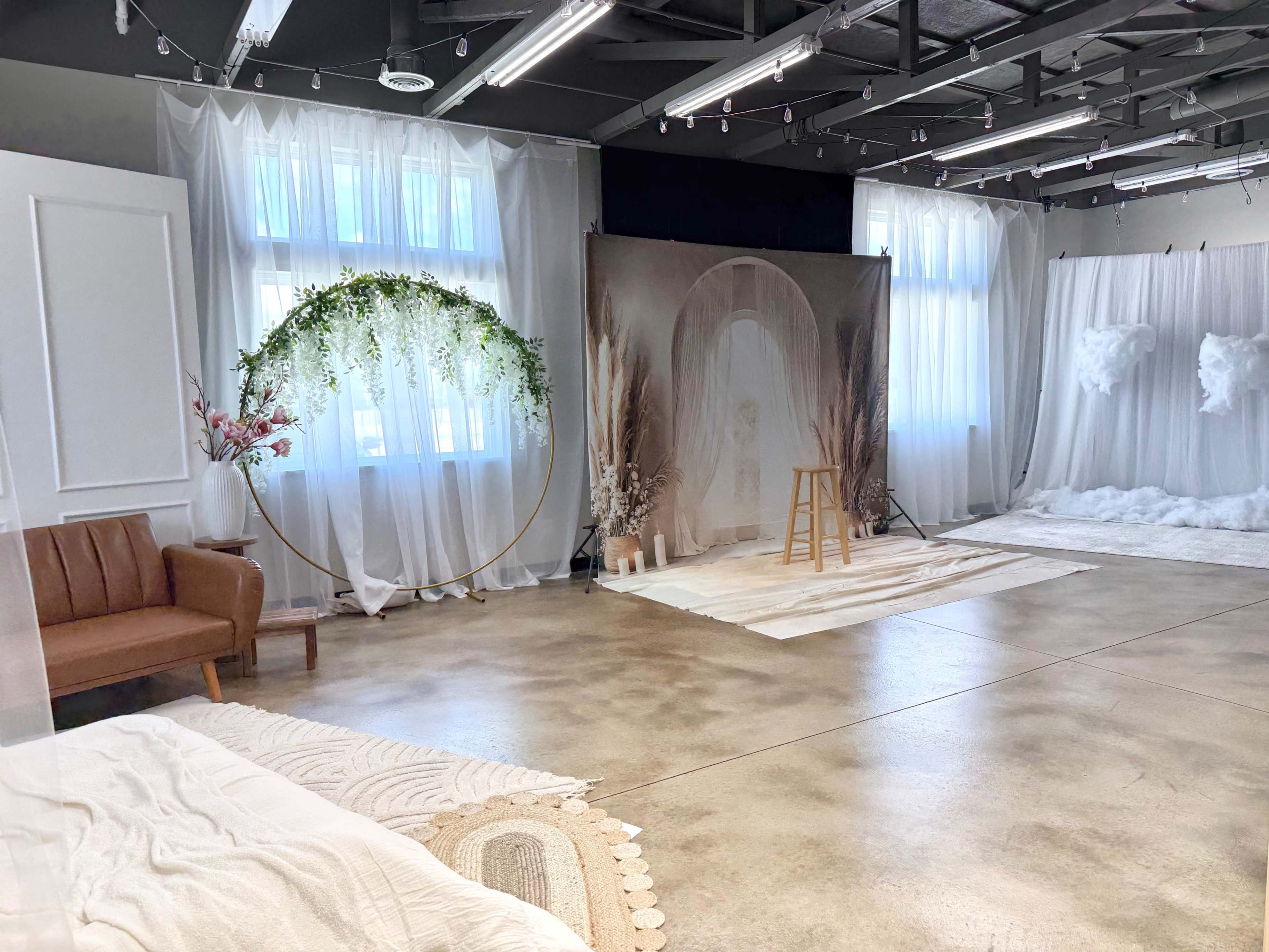 The image shows a well-lit studio with decorative elements including a circular floral arch, a stool, and several backdrop displays against a concrete floor.