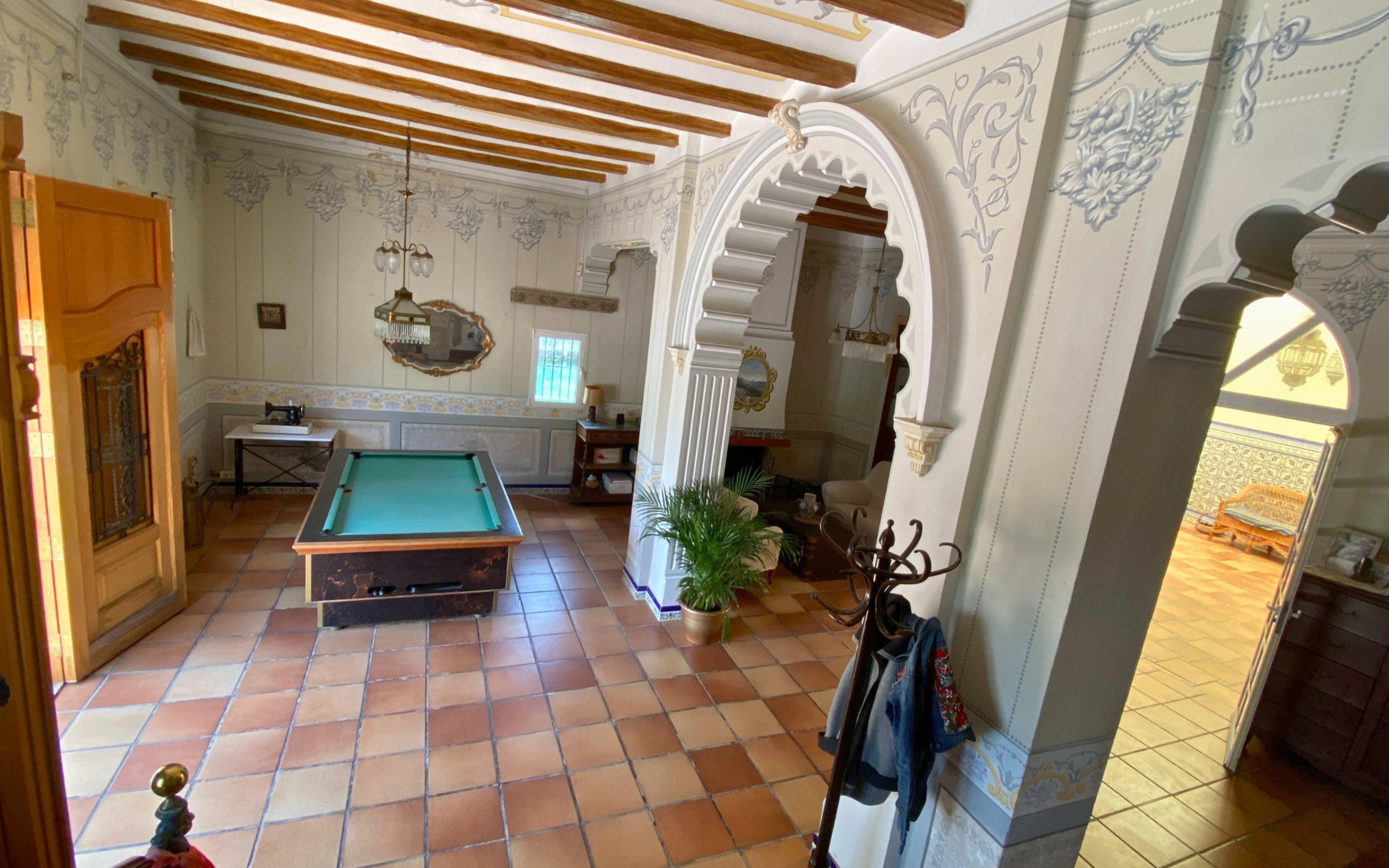 The interior of a spacious room features a pool table, decorative wall details, and tile flooring with wooden beams overhead.