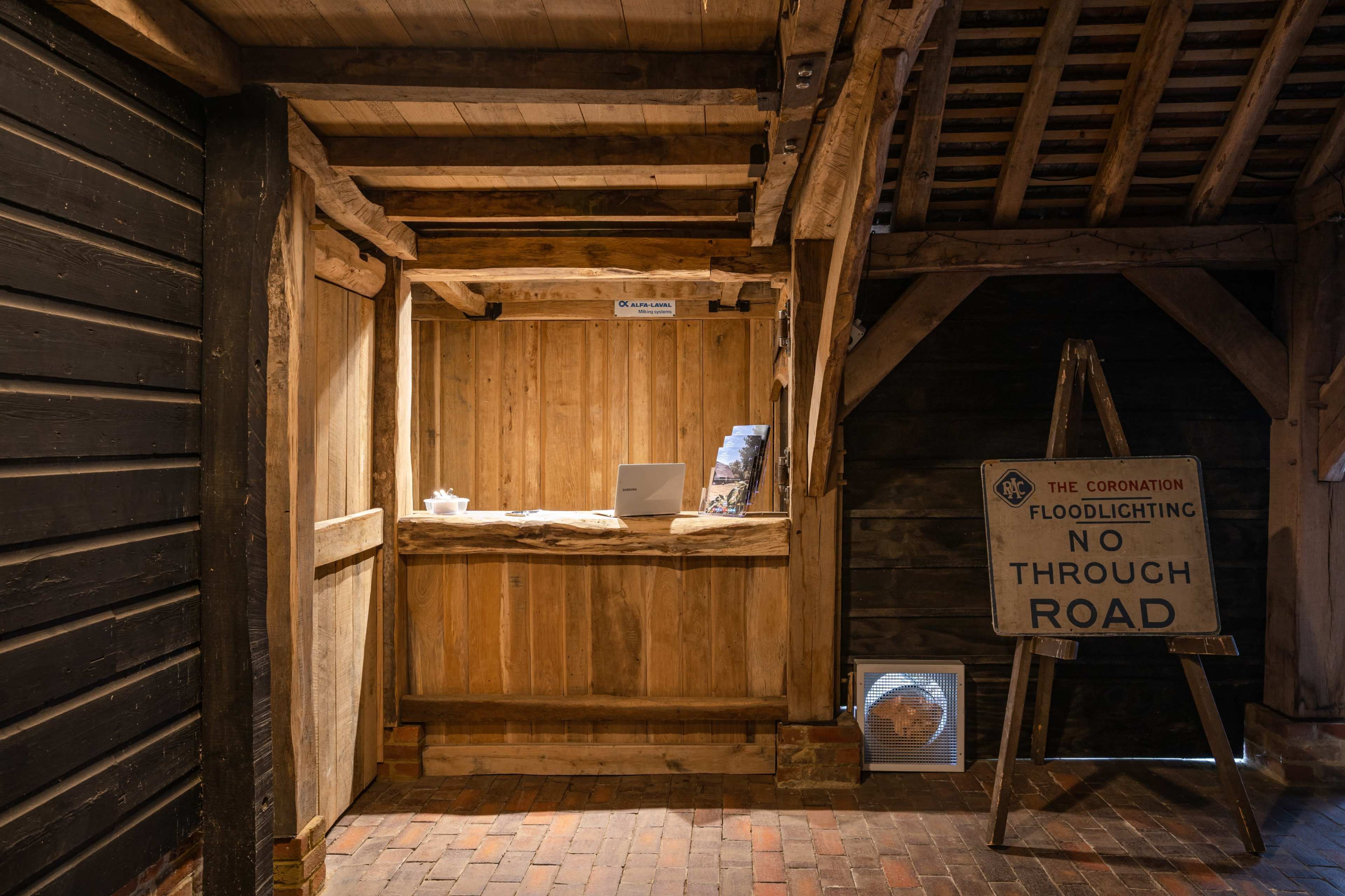 A wooden reception area with a desk, a fan on the floor, and a sign reading "NO THROUGH ROAD" propped against a wall.