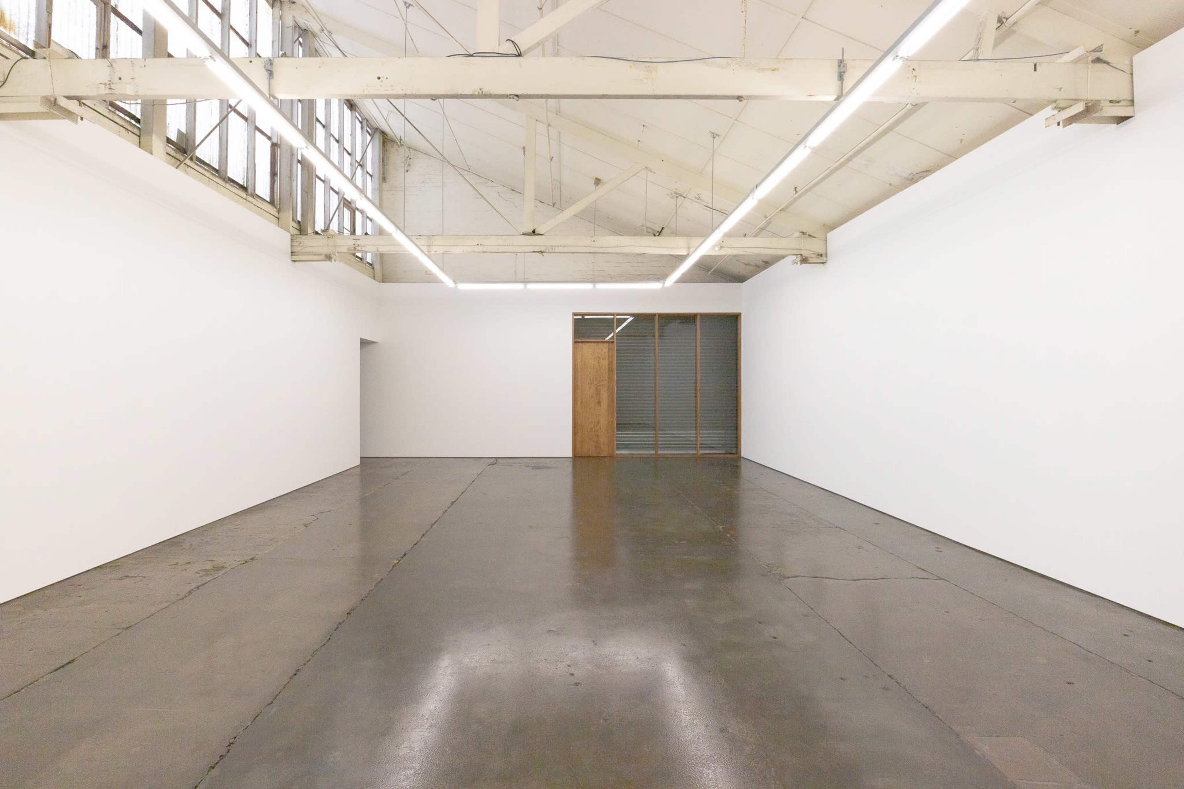 The image shows a spacious, empty gallery with high ceilings, large windows, and polished concrete floors.