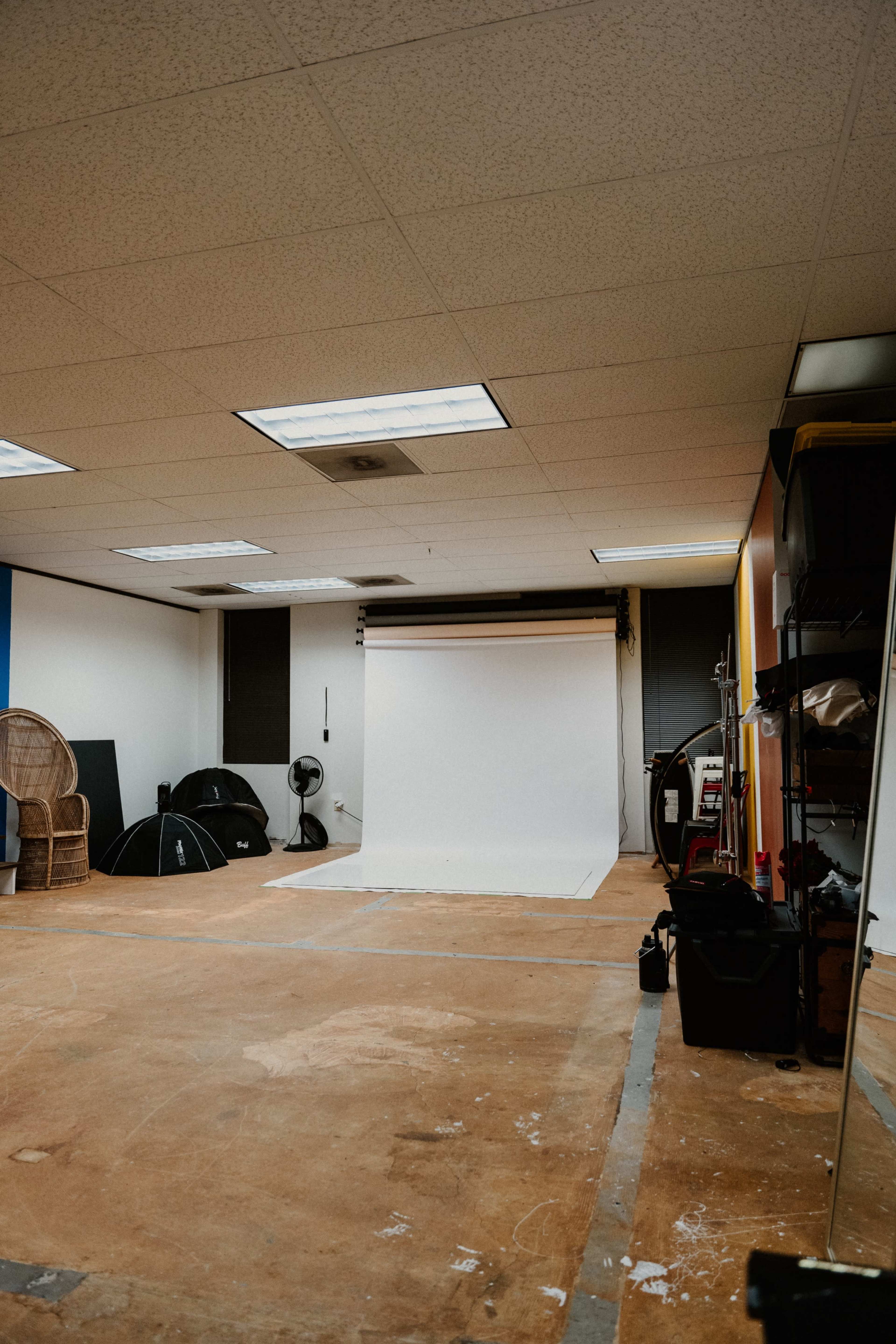 An empty photography studio with a white backdrop, scattered equipment, and chairs arranged along the walls.