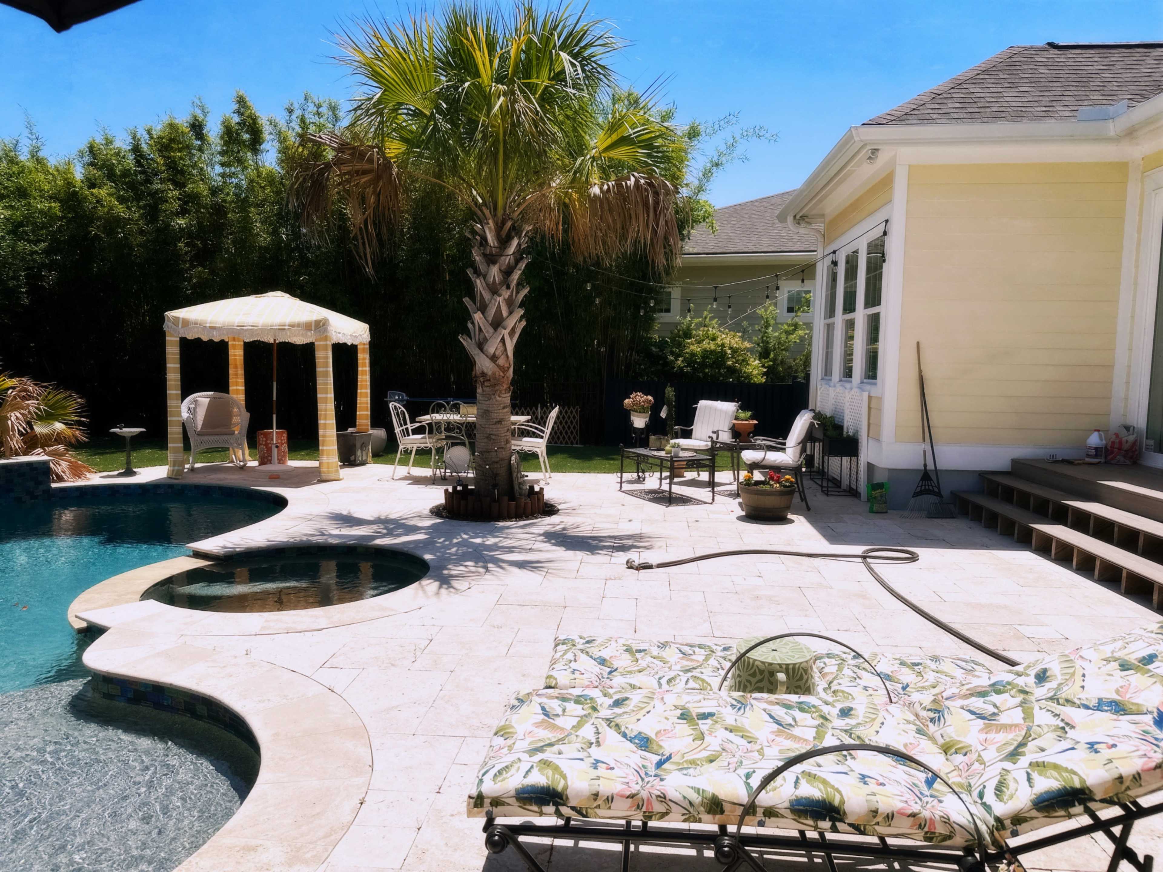 The image shows a backyard pool area with a lounge chair, a palm tree, a cabana, and various seating arrangements around the pool.
