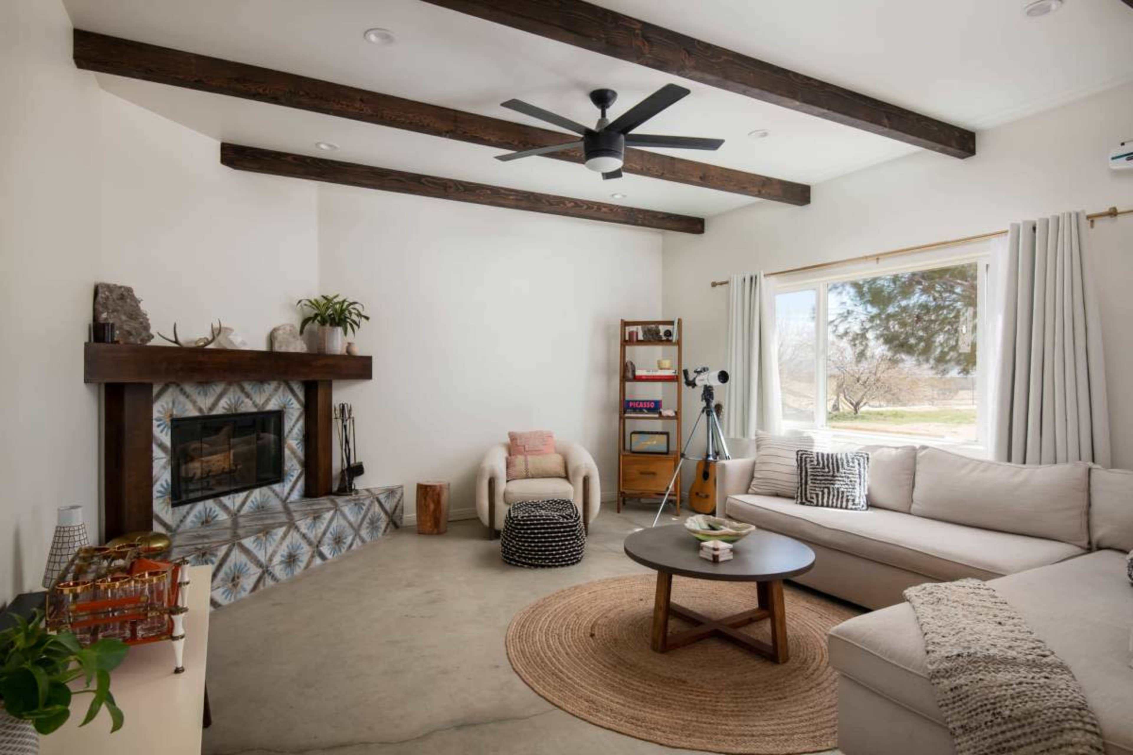 A minimalistic living room with a sectional sofa, a circular coffee table, a fireplace, and a large window allowing natural light to enter.