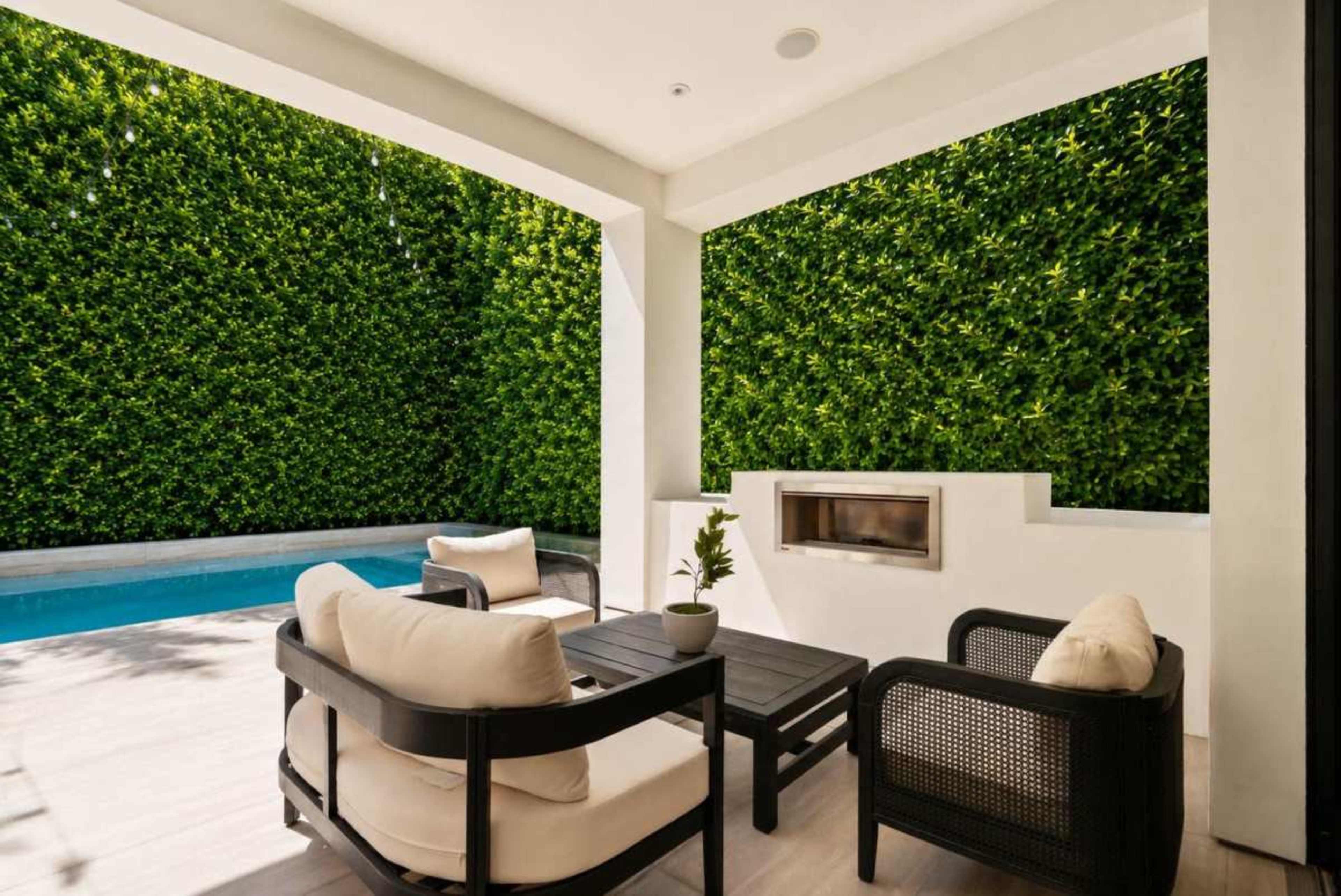 A modern outdoor patio features two chairs and a table, with a pool visible and a vertical green wall in the background.