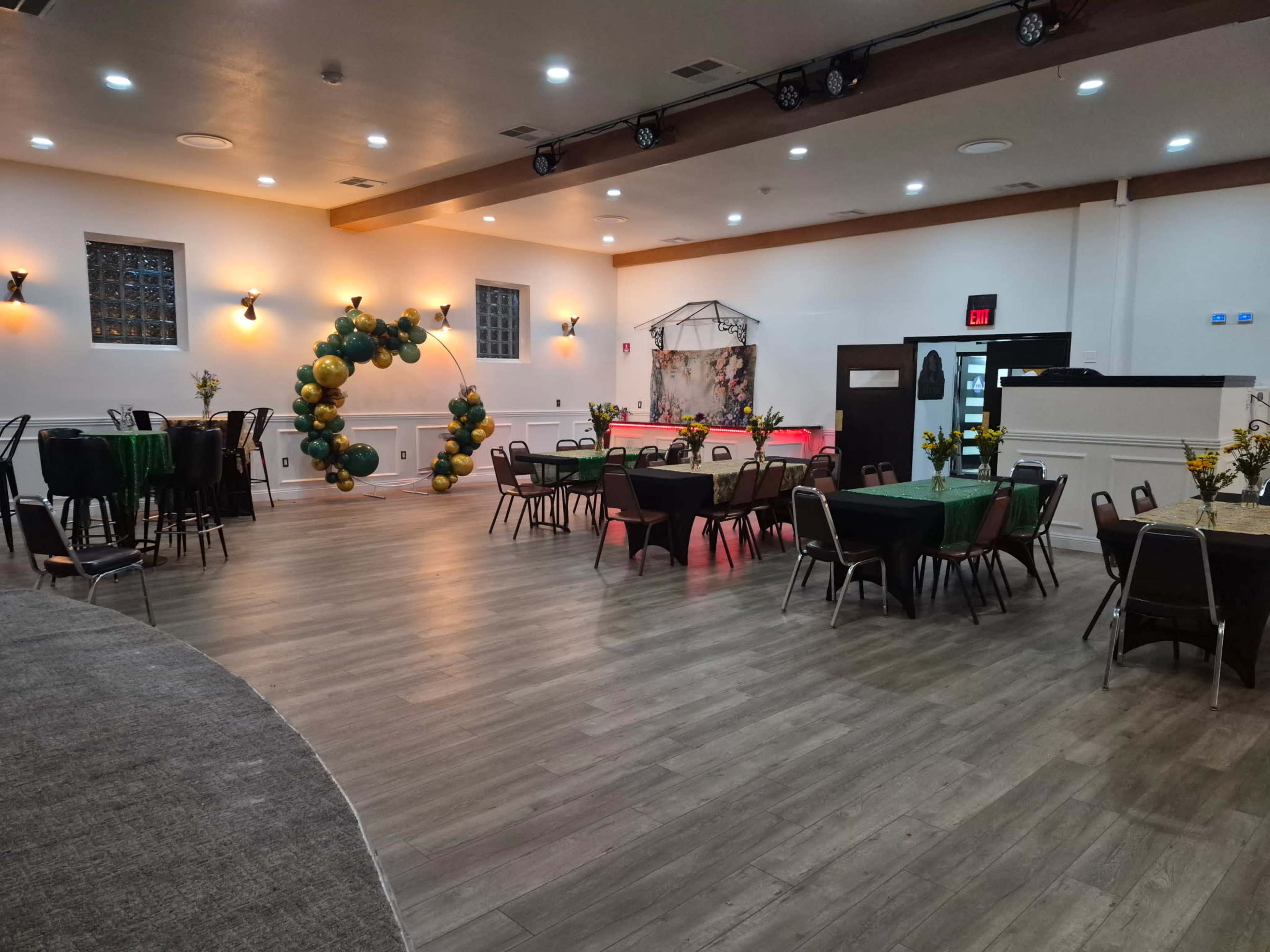 The image shows a banquet hall set up with several round tables, decorated with black and green tablecloths, and an arch made of balloons in the background, ready for an event.