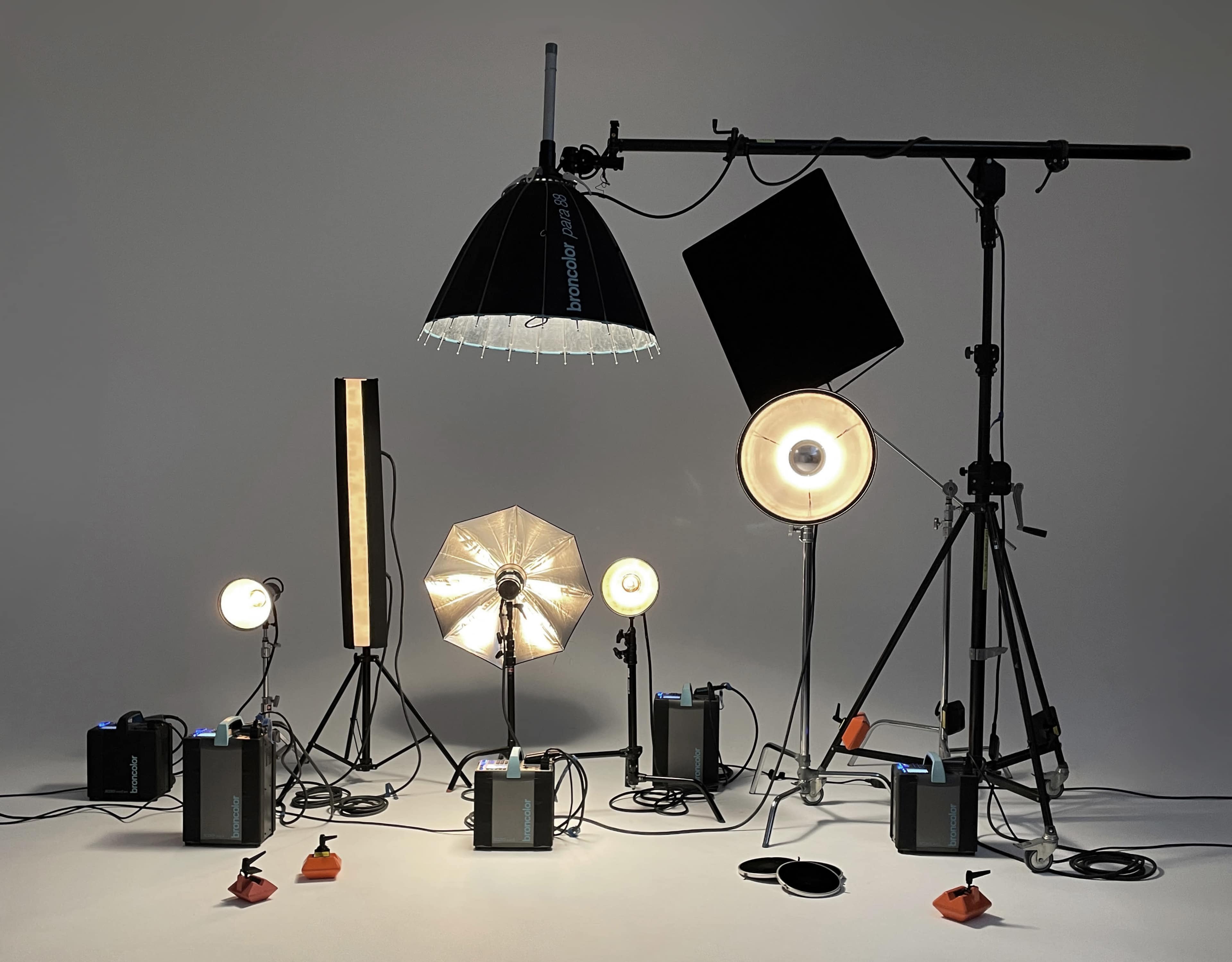 A photography studio setup featuring various lighting equipment, including softboxes, spotlights, and reflectors arranged on tripods.