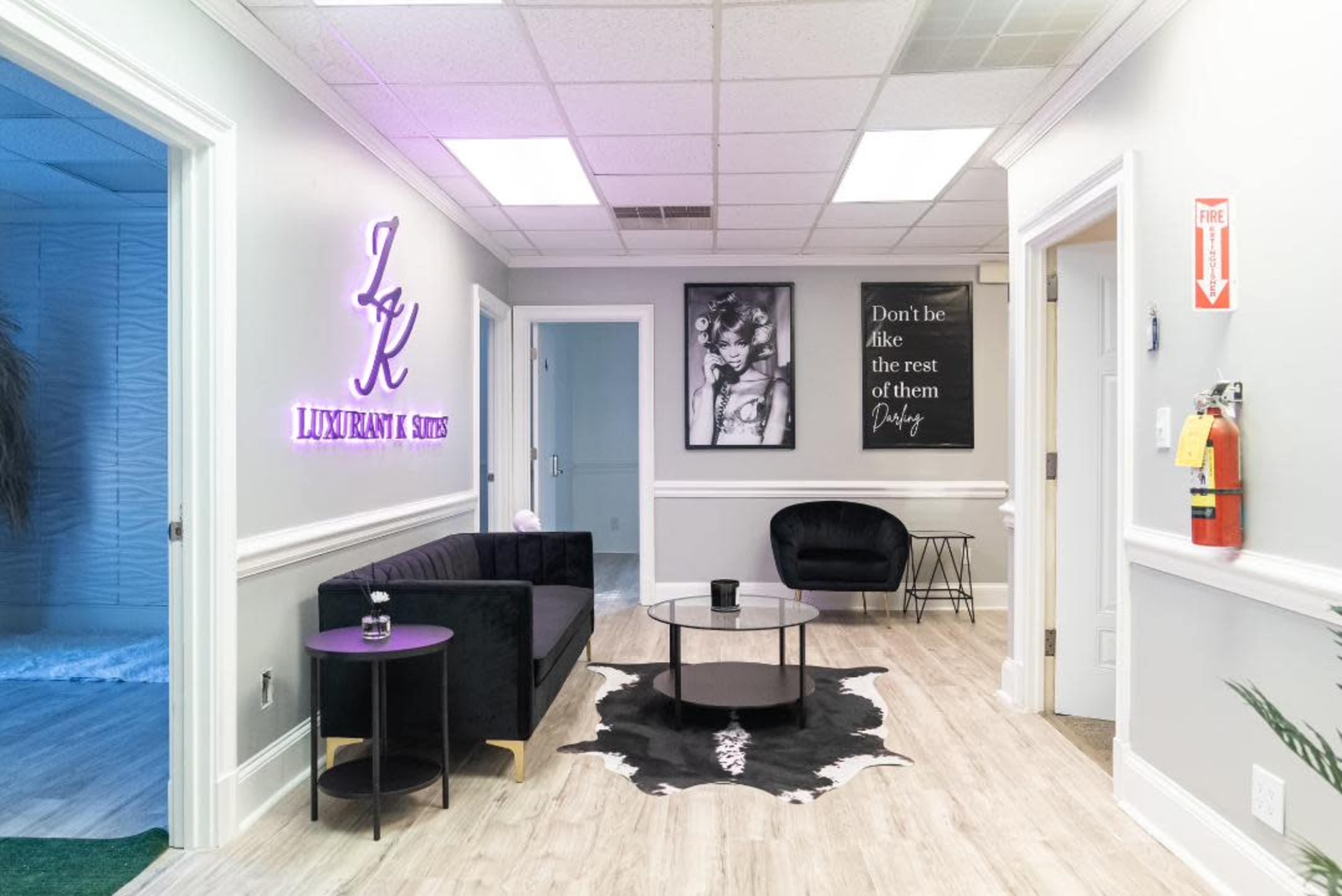 A modern waiting area with a black sofa, a round coffee table, and framed artworks on the walls, featuring a neon sign displaying "LUXURIANT & STYLES."