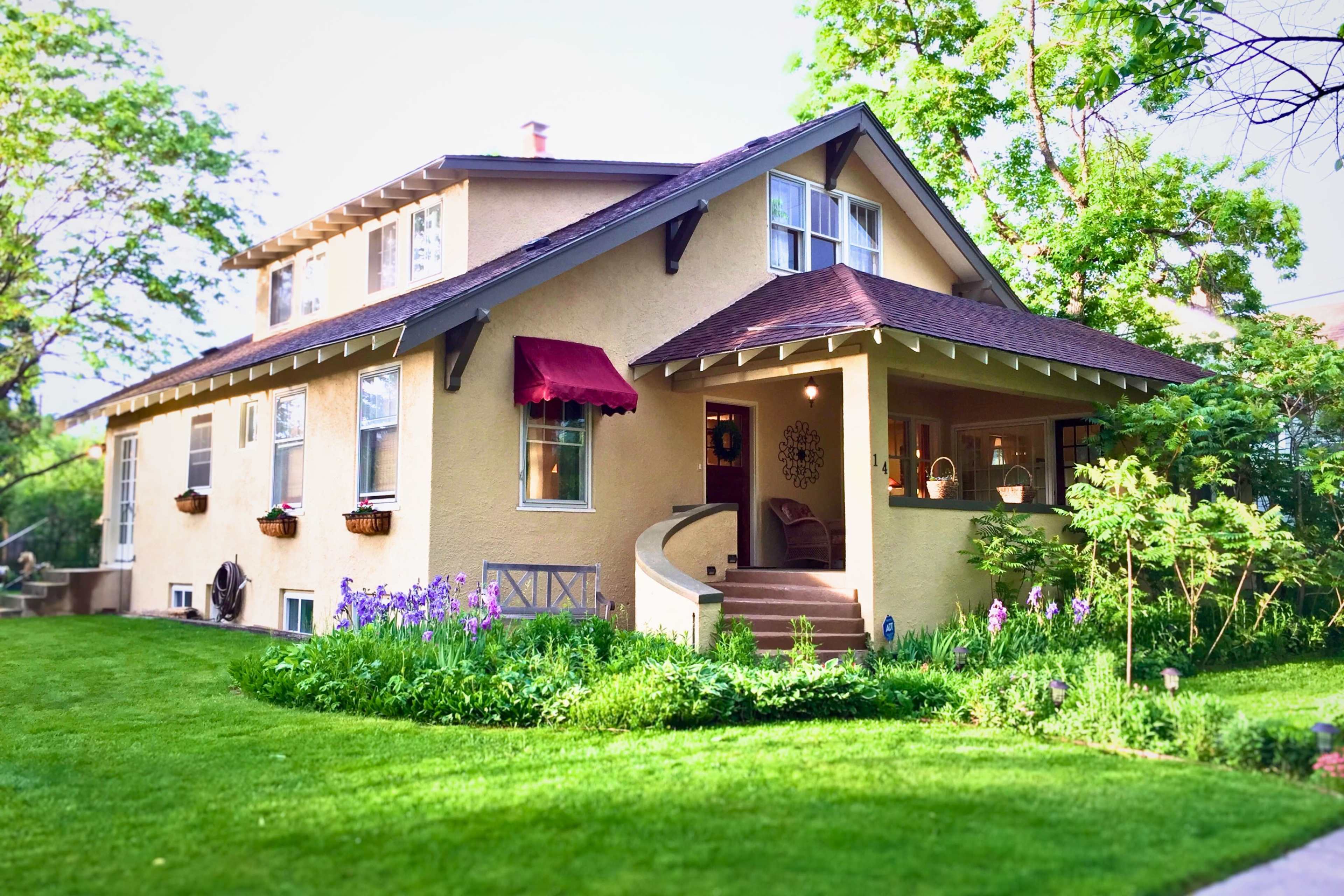 A two-story house with a sloped roof, a covered porch, and colorful flower beds surrounded by a well-maintained lawn.