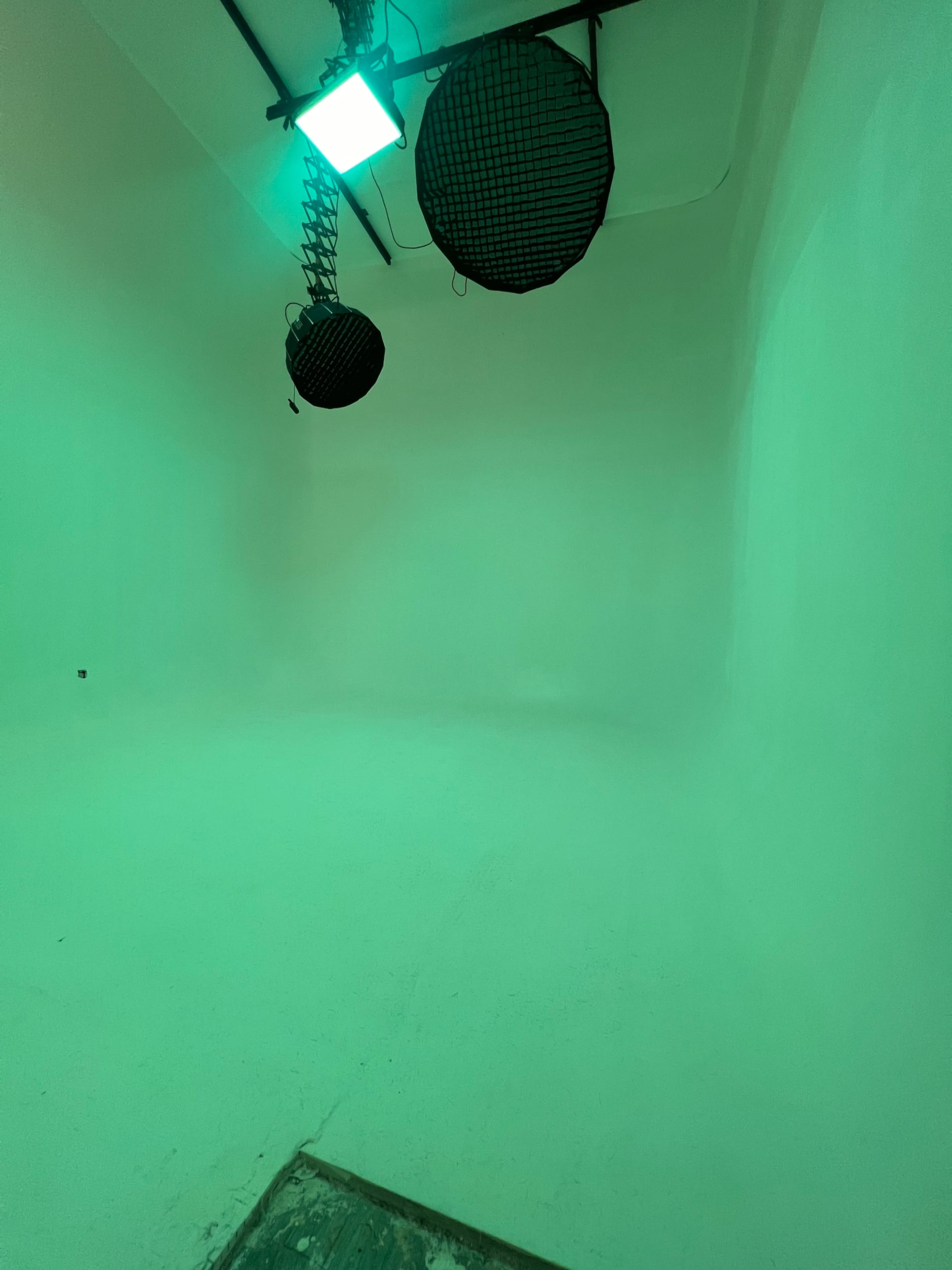 A minimalist studio space with two black lights hanging from the ceiling and green lighting illuminating the white walls.