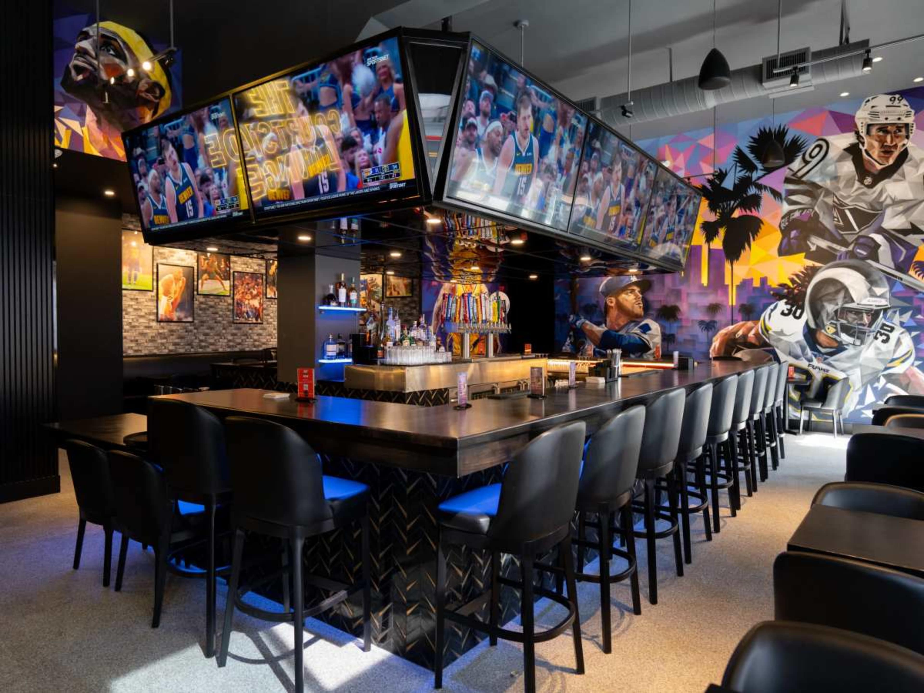 The image shows a modern sports bar with multiple large screens displaying games, surrounded by colorful wall murals and a stylish bar area.