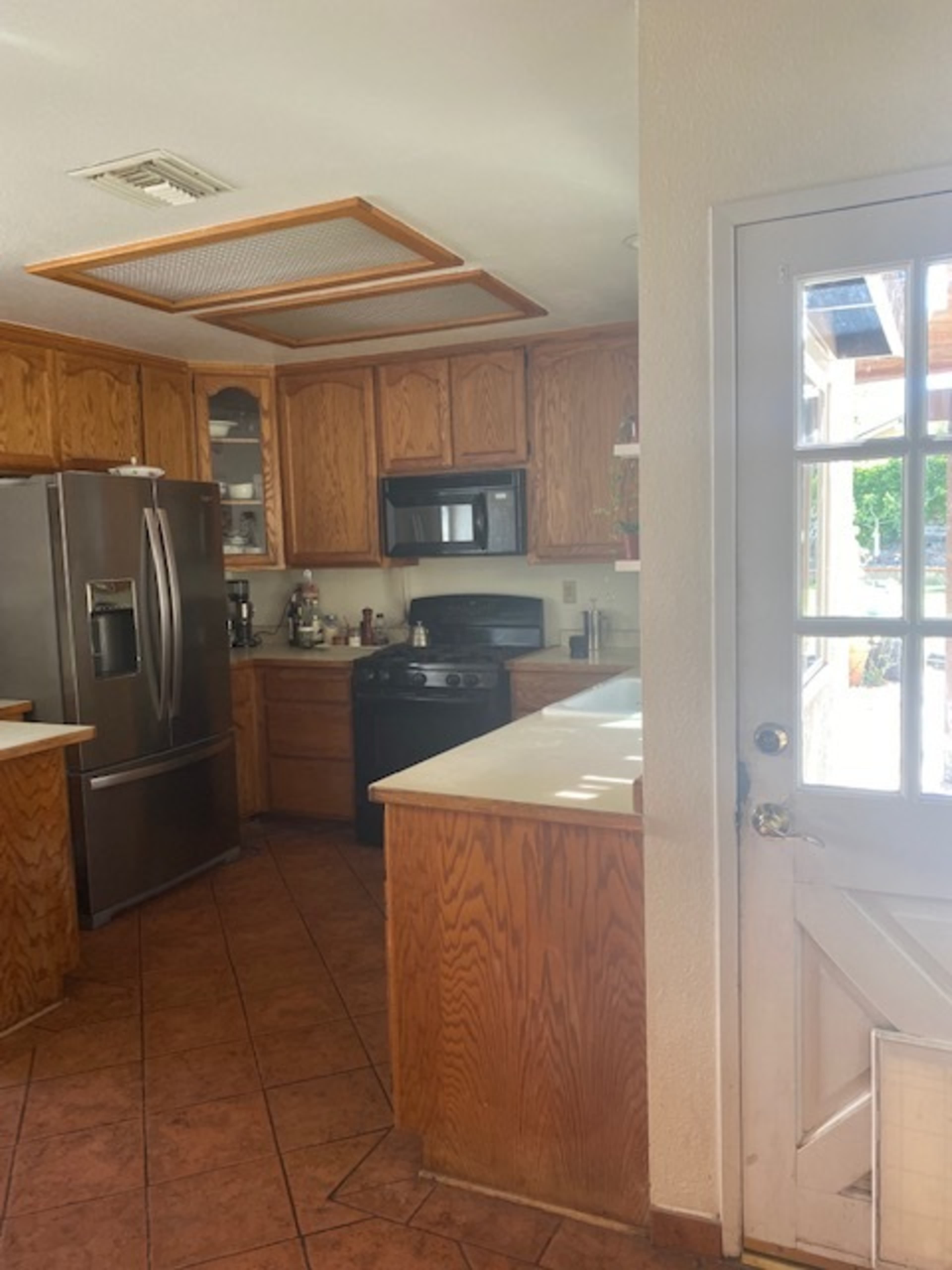 A kitchen with wooden cabinets, a stainless steel refrigerator, and a door leading outside.