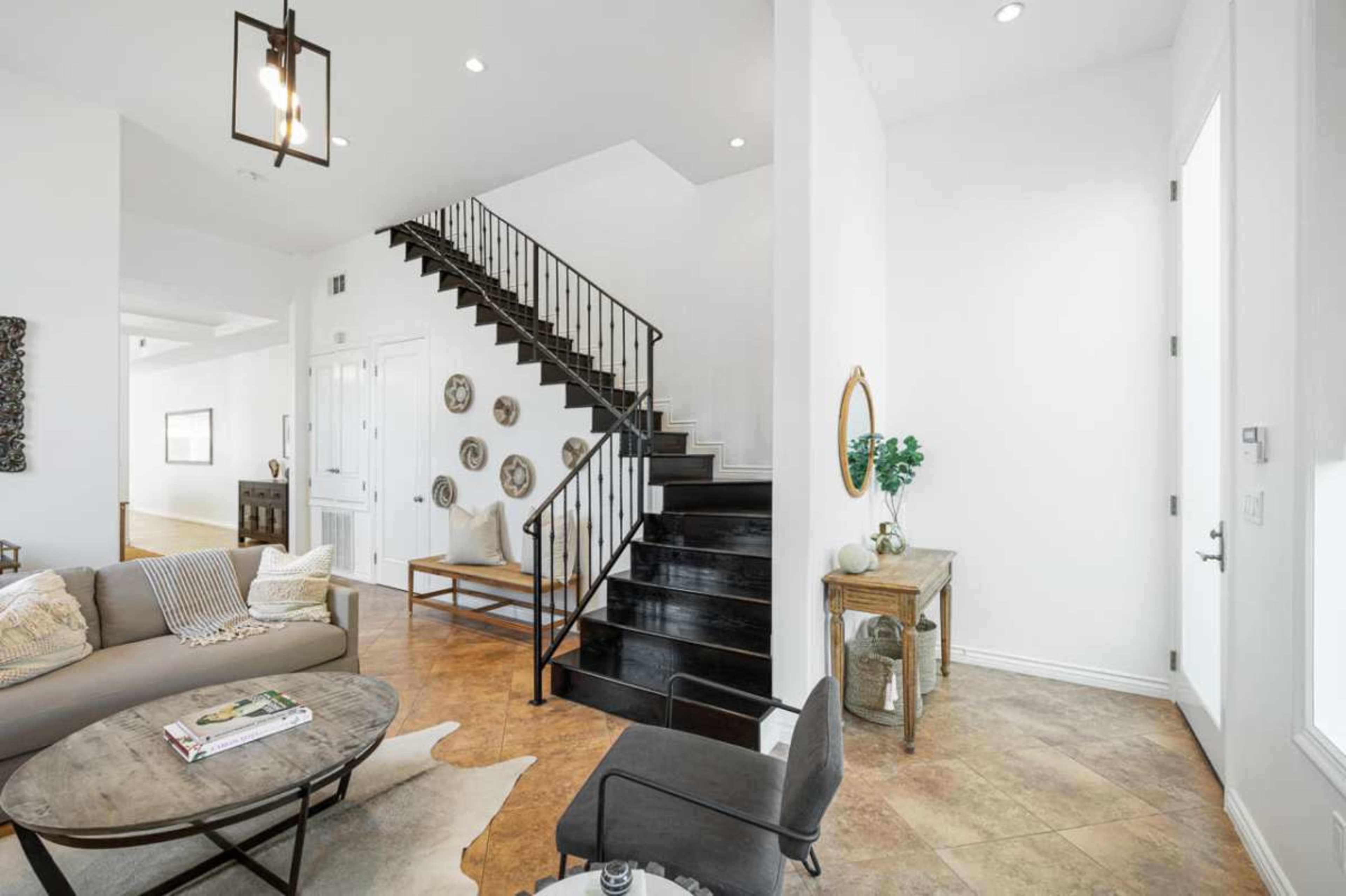 The image shows a modern living space featuring a staircase with a black railing, a light-colored sofa, and a small table next to a doorway.
