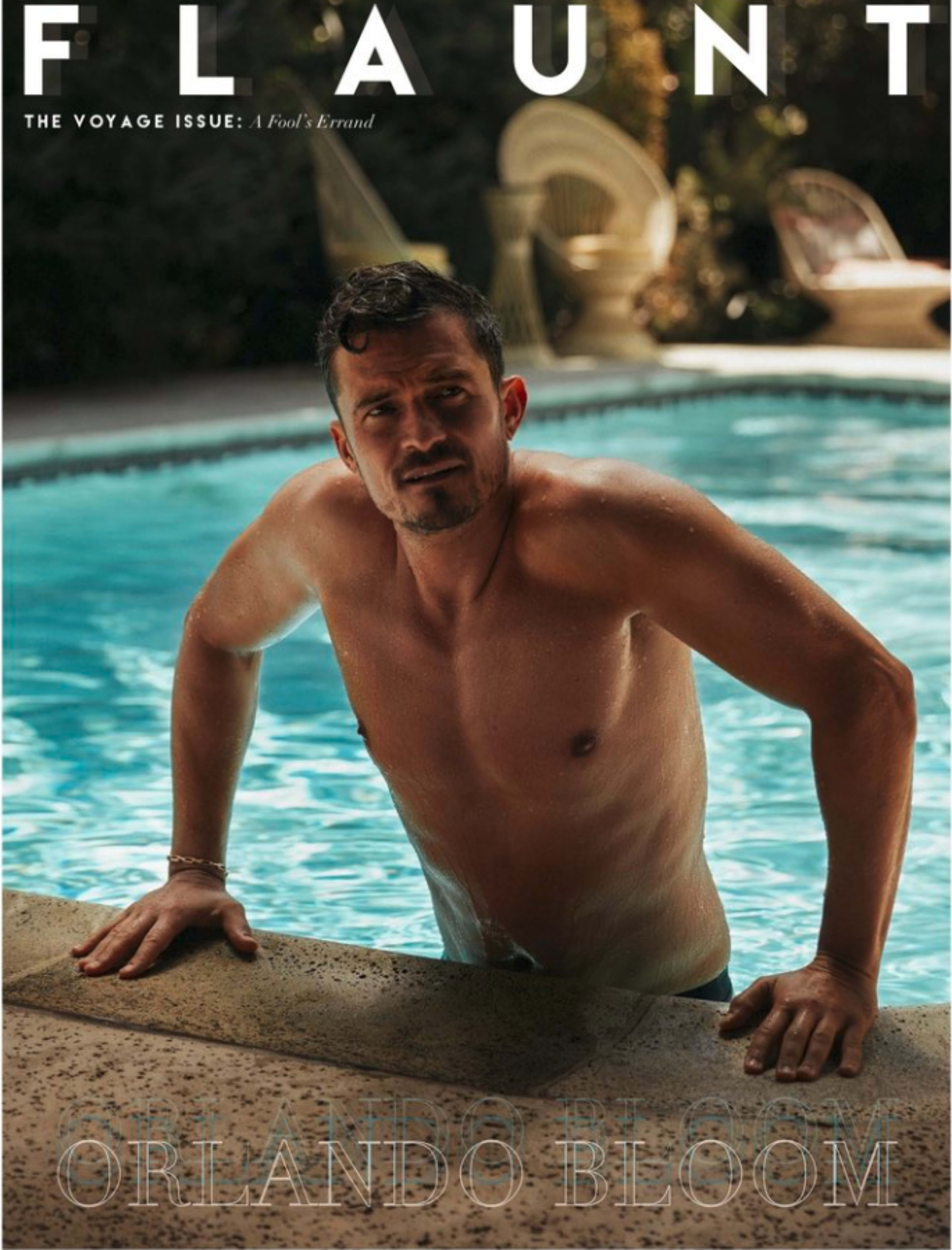A shirtless man is perched on the edge of a pool, leaning slightly forward, surrounded by greenery.