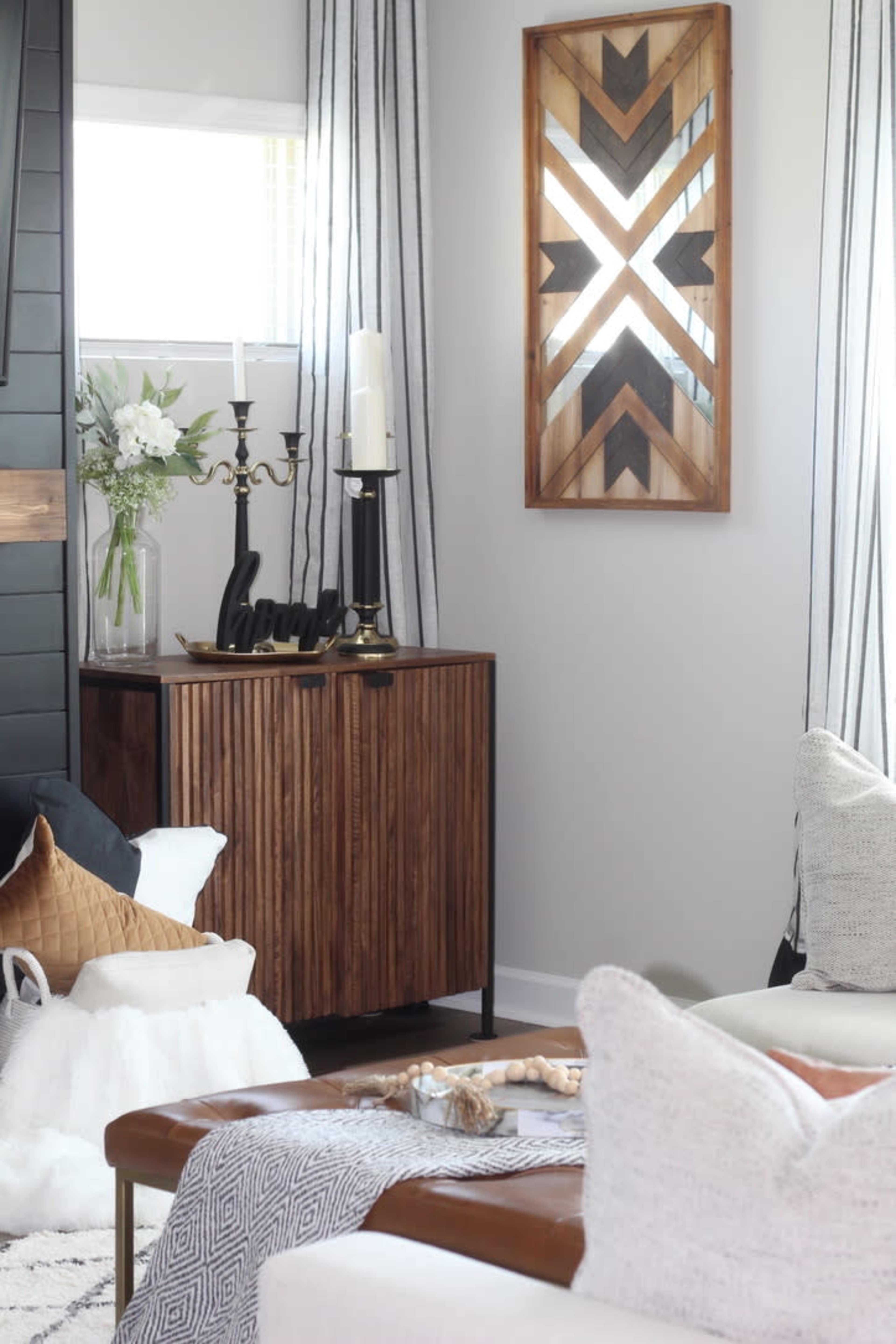 A modern living room features a wooden sideboard adorned with decorative items, a geometric wall art piece, and contrasting light and dark furnishings.