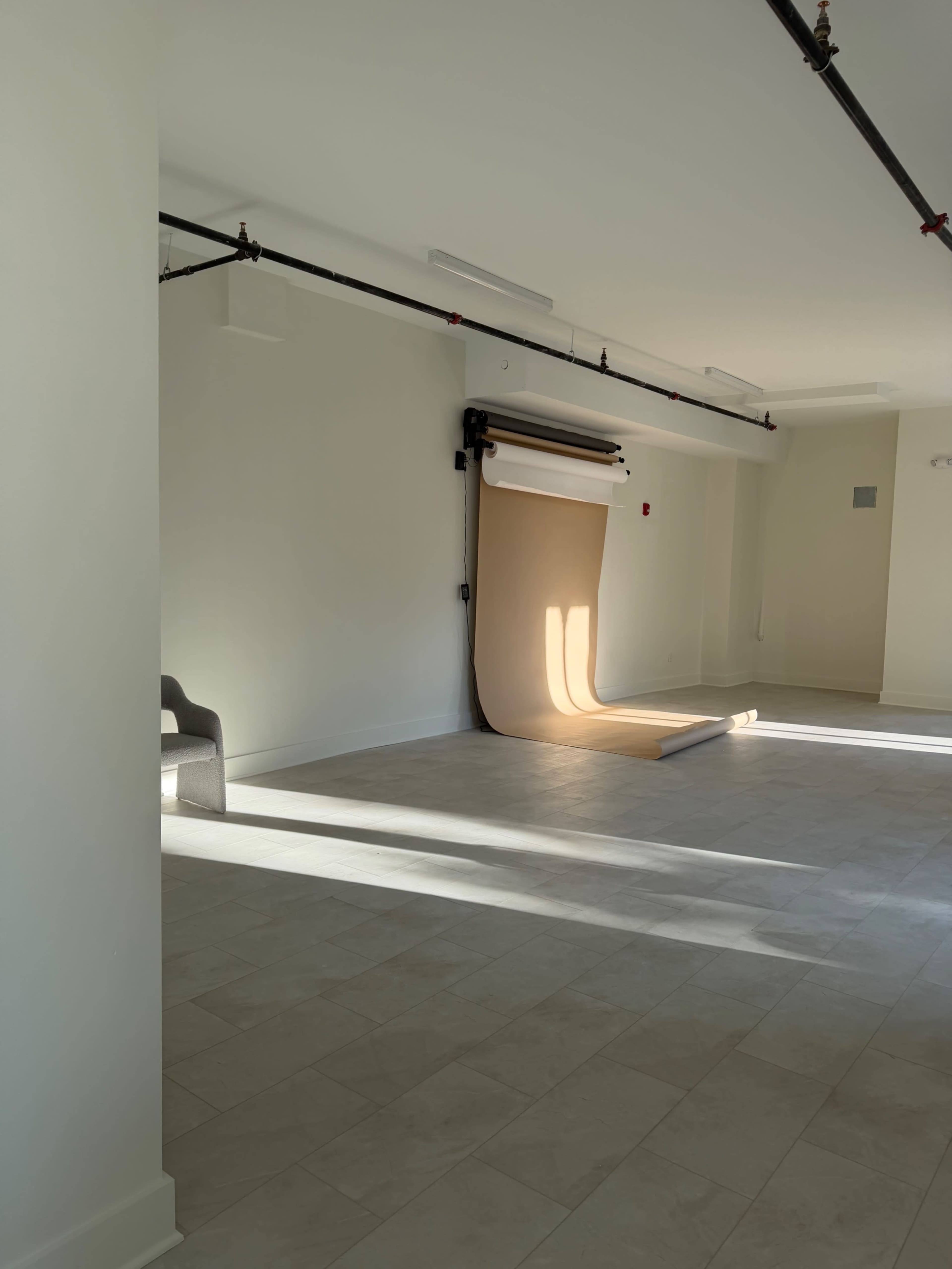 The image shows an empty studio space with a large roll of backdrop paper and natural light casting shadows on the floor.