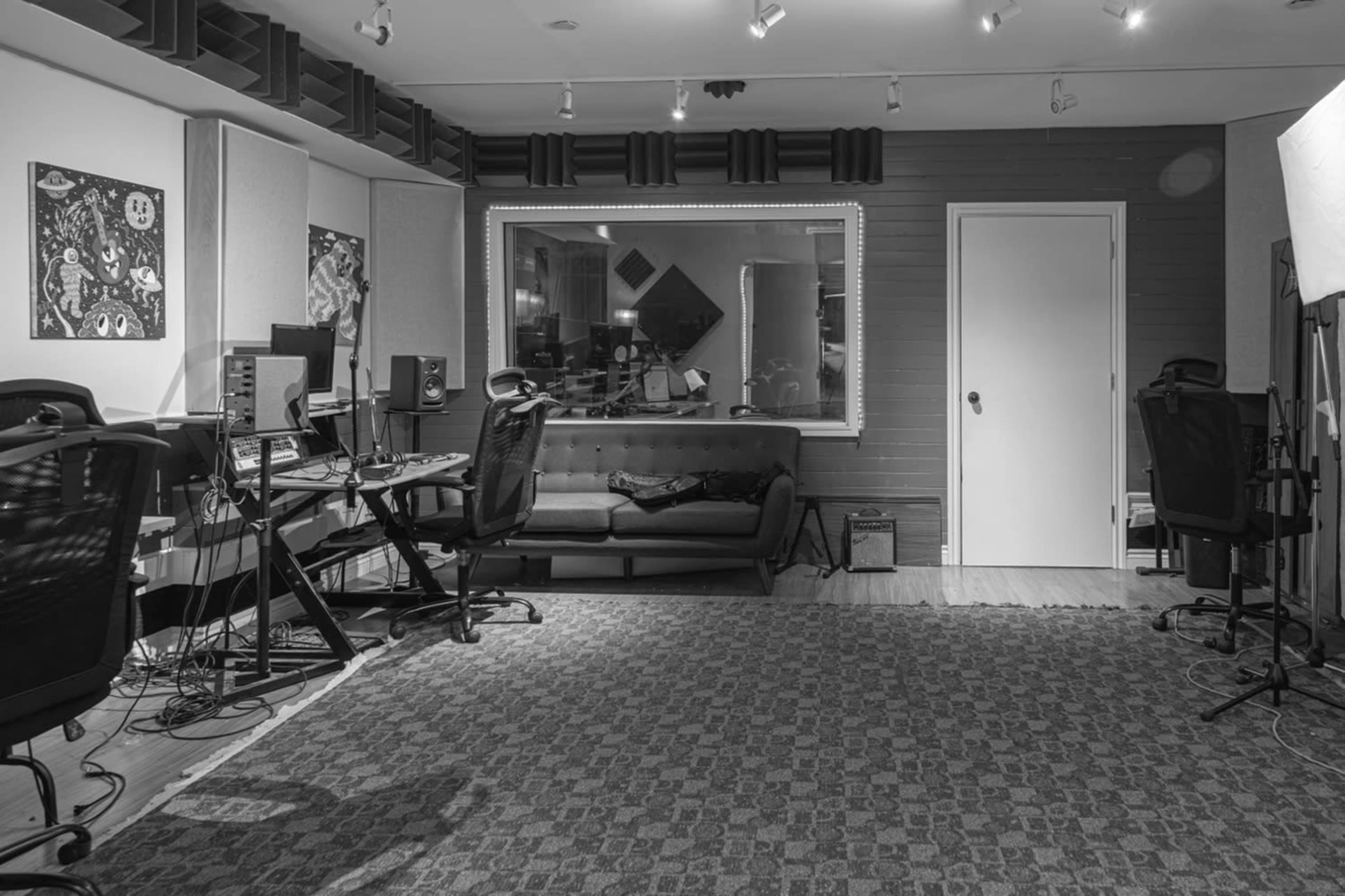 A music recording studio with desks, computer equipment, and a large window overlooking an isolated seating area.