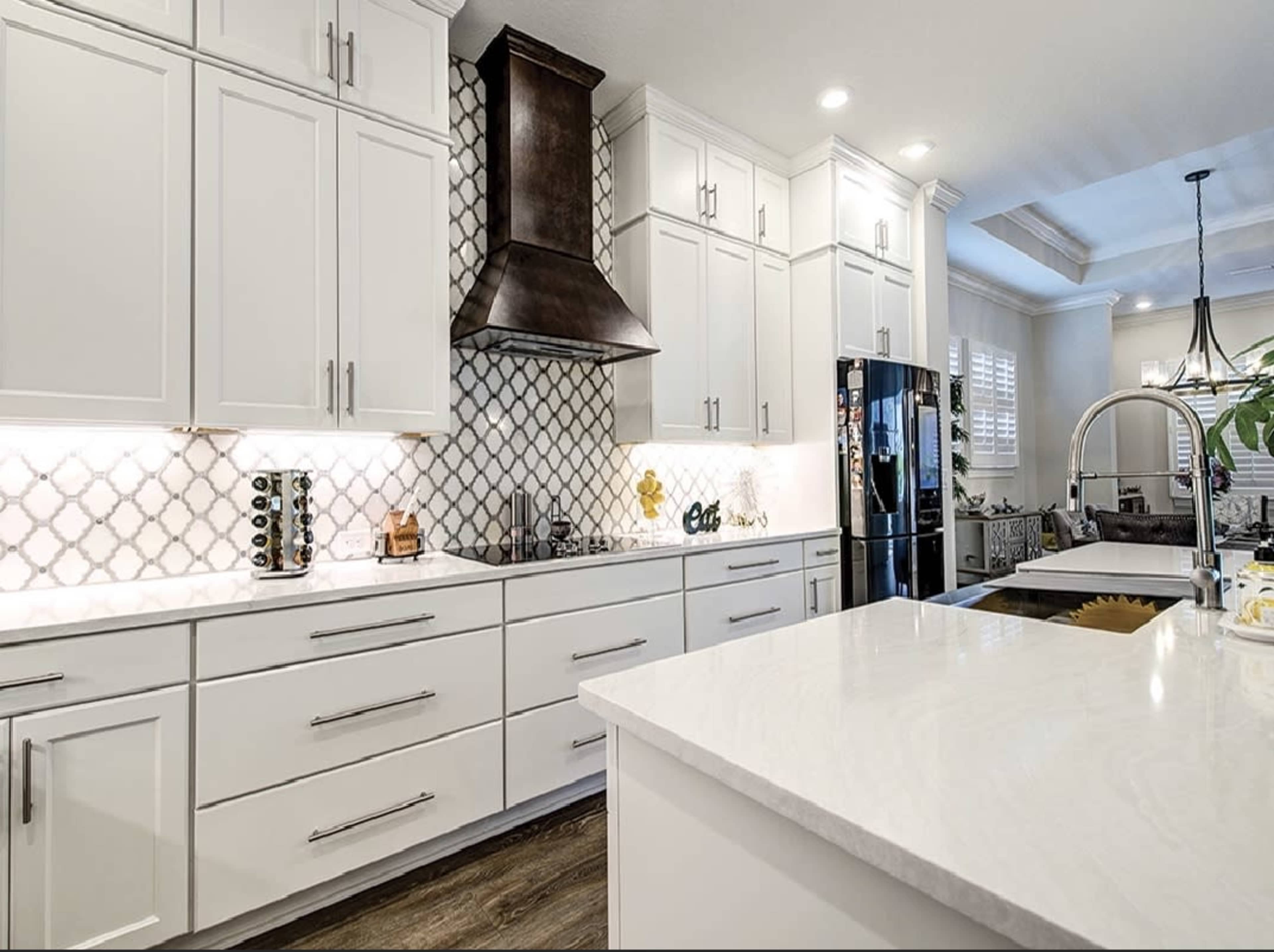 A modern kitchen featuring white cabinetry, a patterned backsplash, a stainless steel range hood, and a large island with a marble countertop.