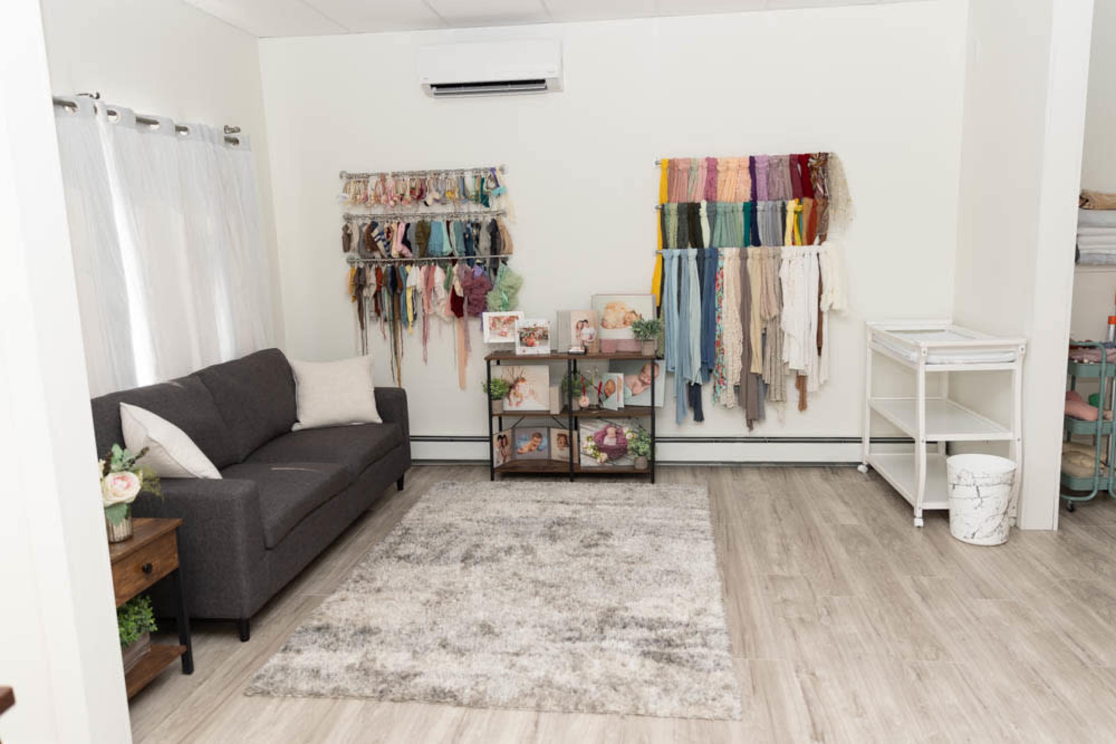 A well-organized room featuring a gray sofa, a rug, and colorful fabric hangings on the walls, along with shelves displaying framed pictures and various items.