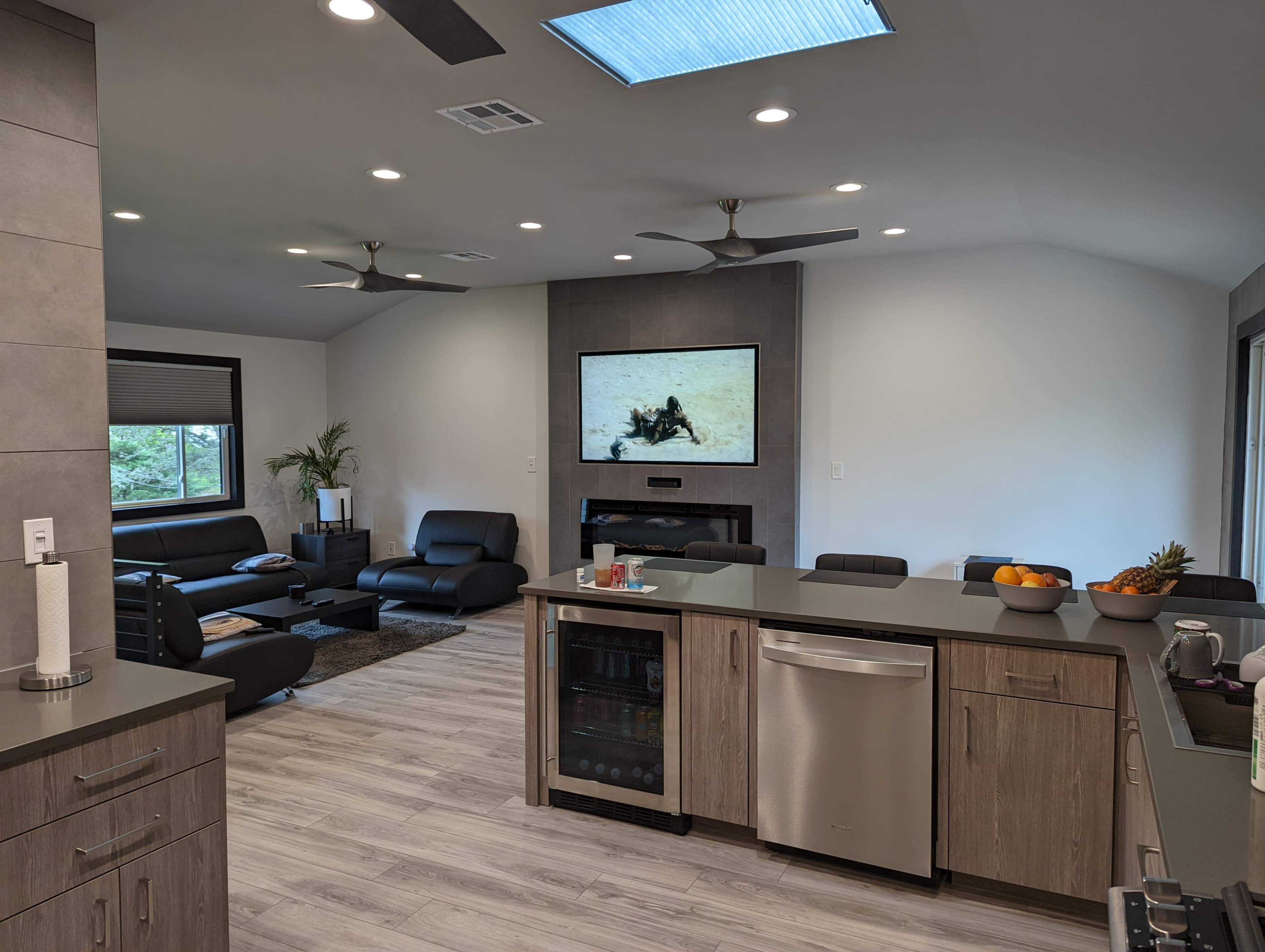 A modern open-concept living space features a kitchen with a gray island, a living area with black seating, and a television mounted on the wall.