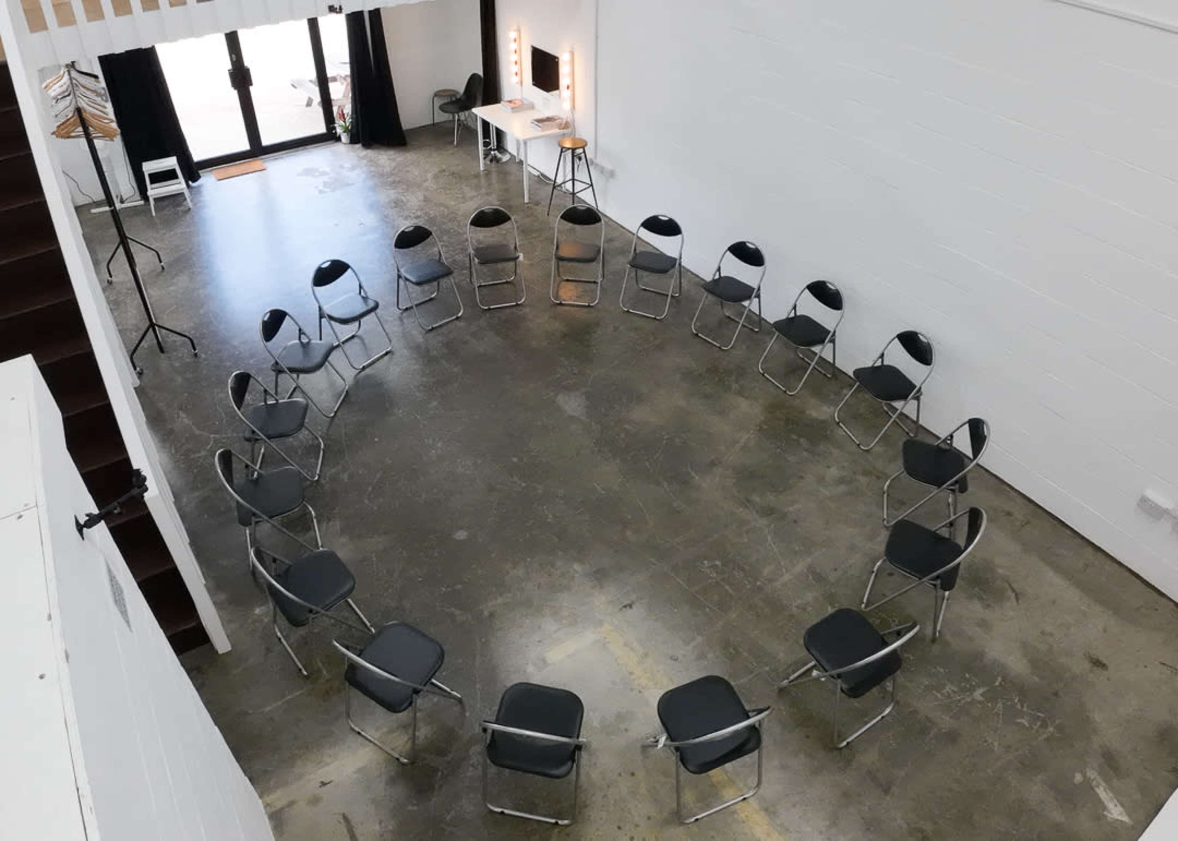 A circular arrangement of metal chairs on a concrete floor within a spacious, brightly lit room.