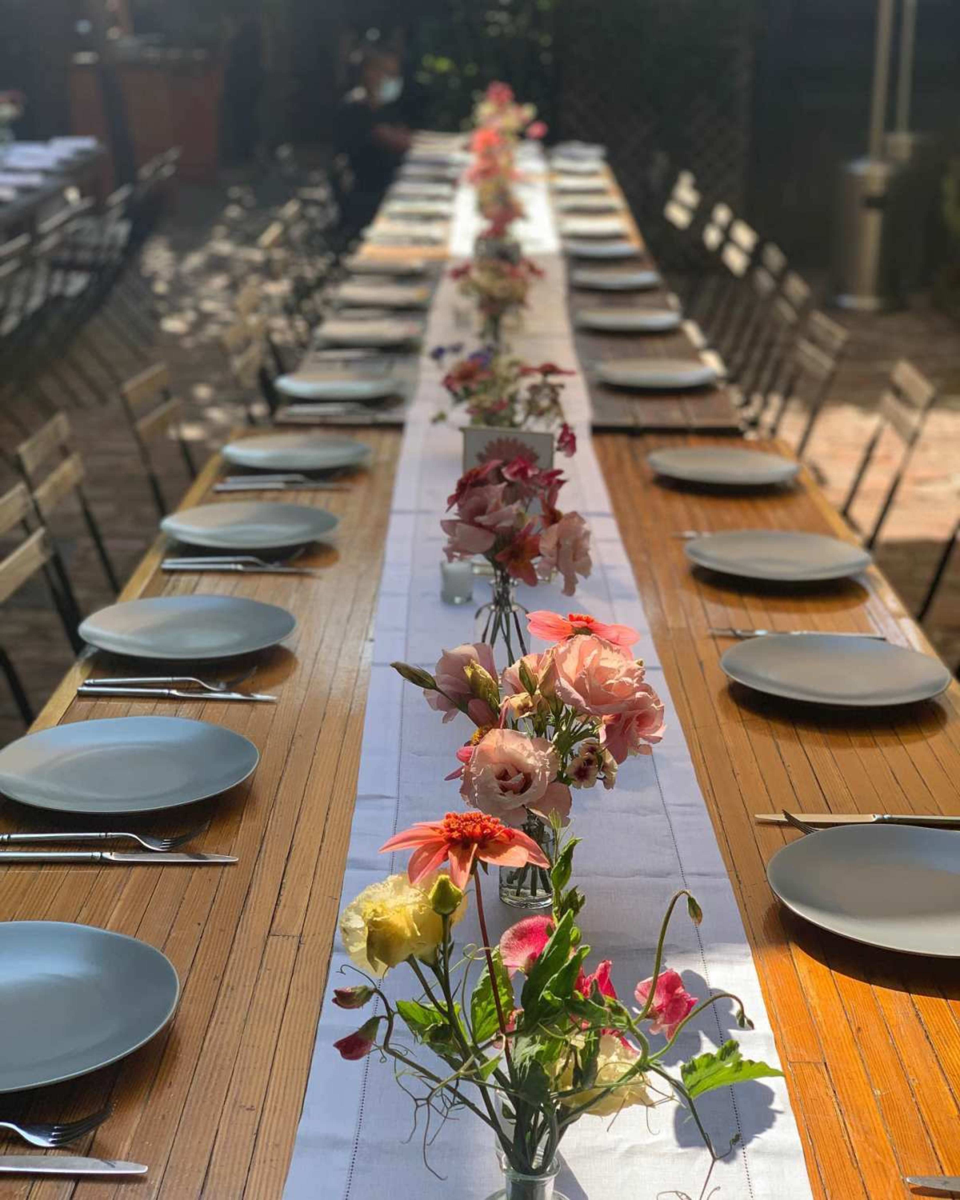 A long wooden dining table is set with empty plates and a floral centerpiece running down the middle.