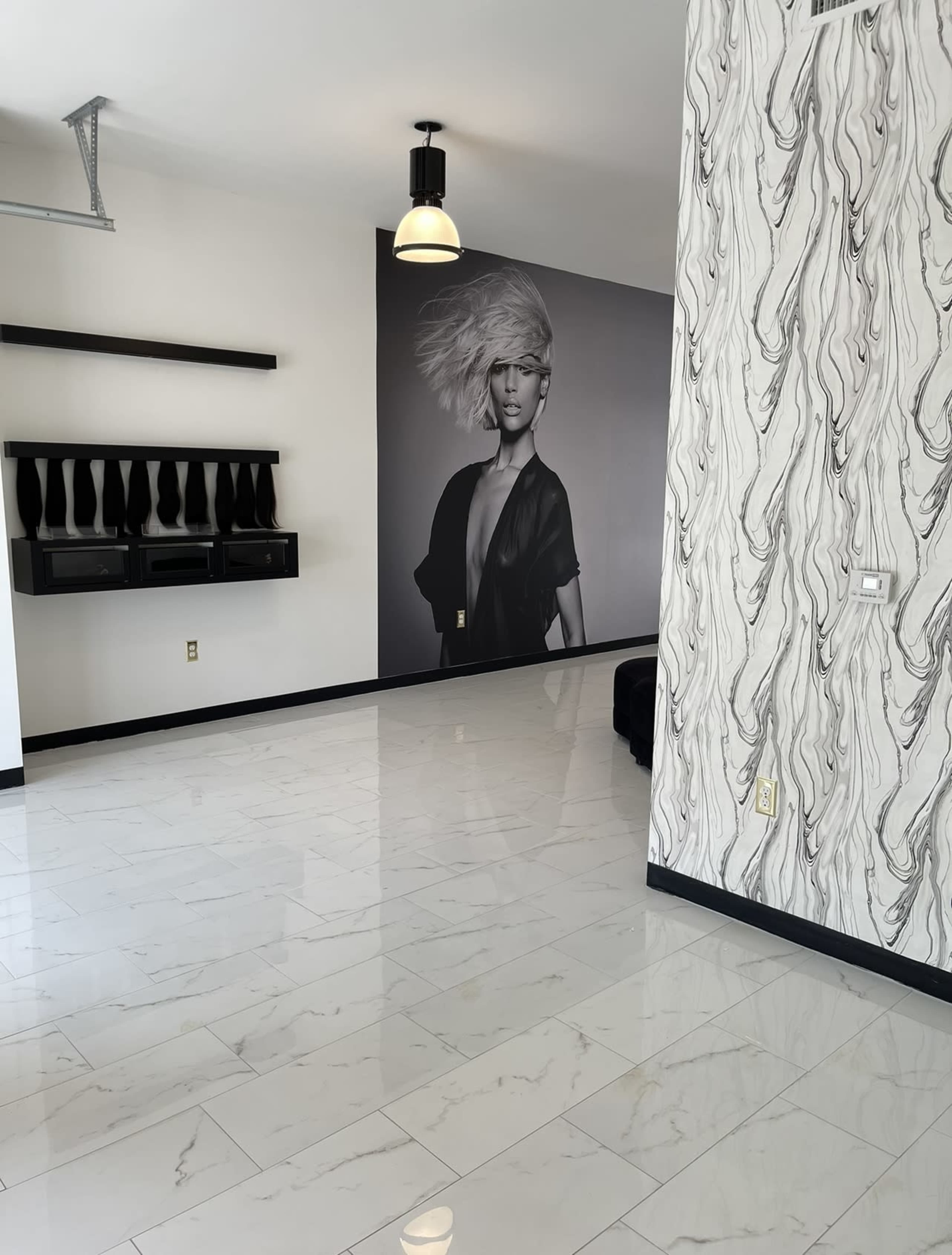The image shows a spacious room with glossy white tile flooring, a patterned wall featuring a large black-and-white portrait of a model, and modern shelving.