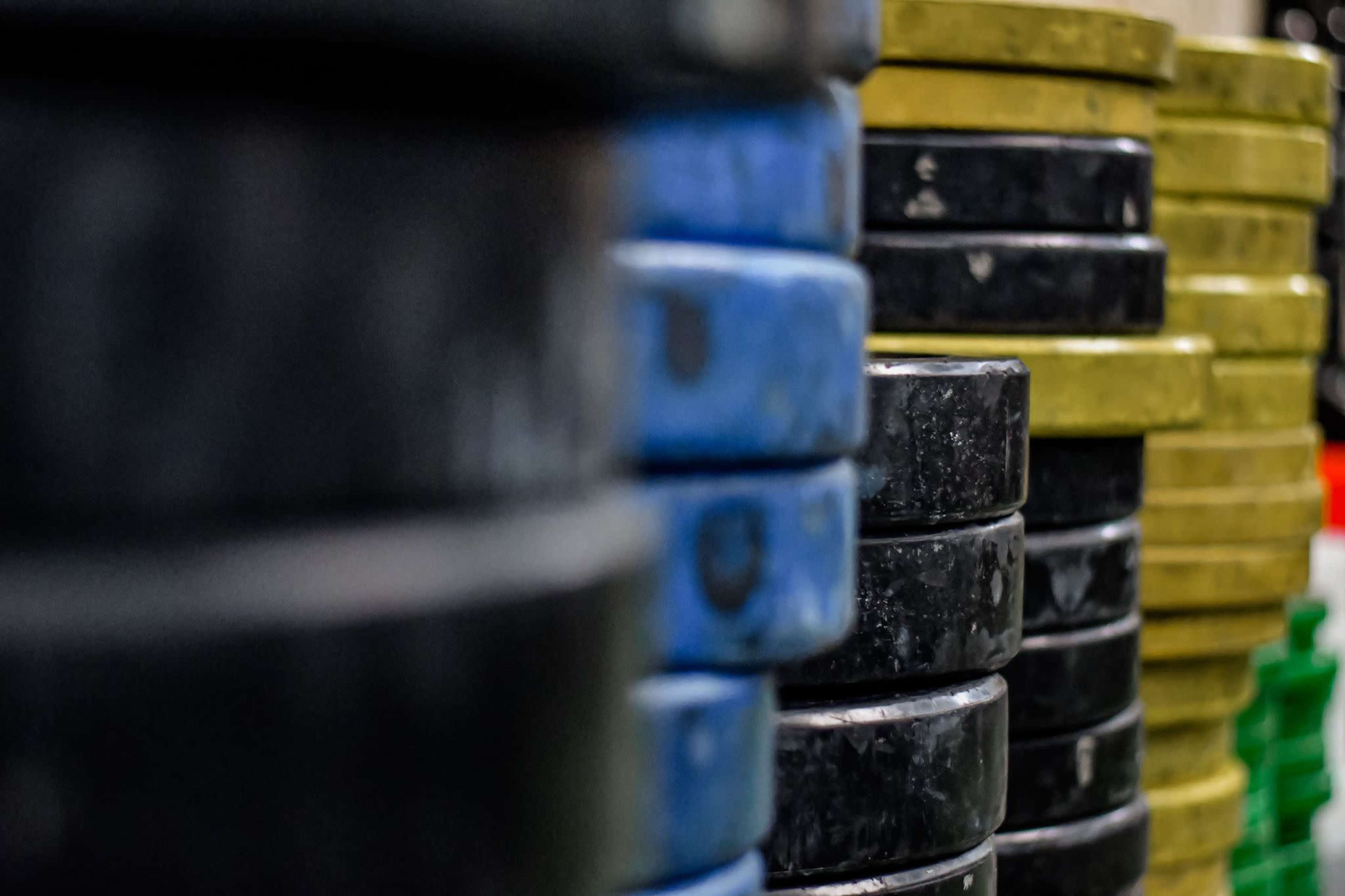 A stack of weightlifting plates in various colors, including black, blue, and yellow, arranged neatly in a gym setting.