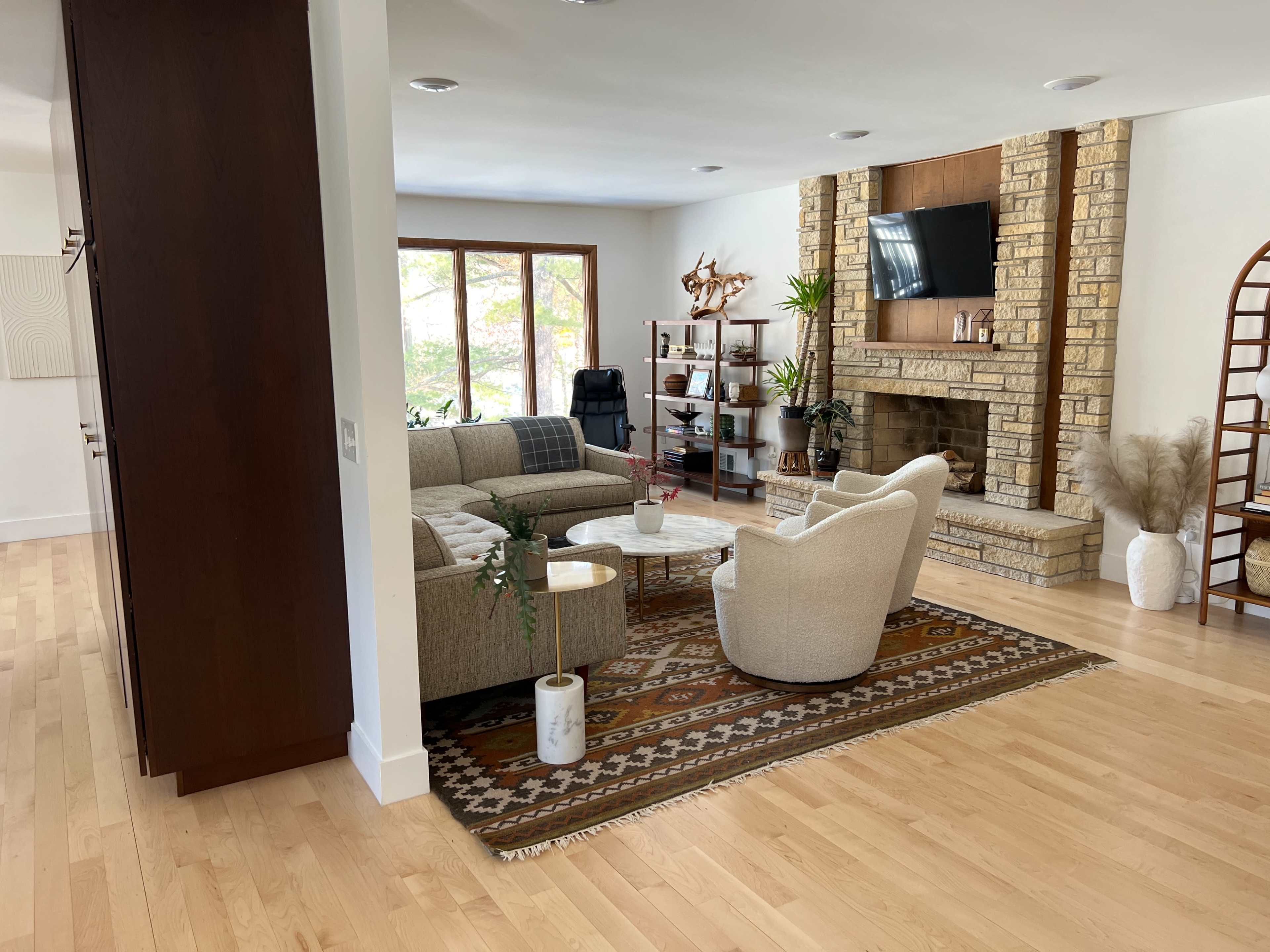 A modern living room featuring a stone fireplace, a cozy seating arrangement with two armchairs and a sofa, and a large window allowing natural light.
