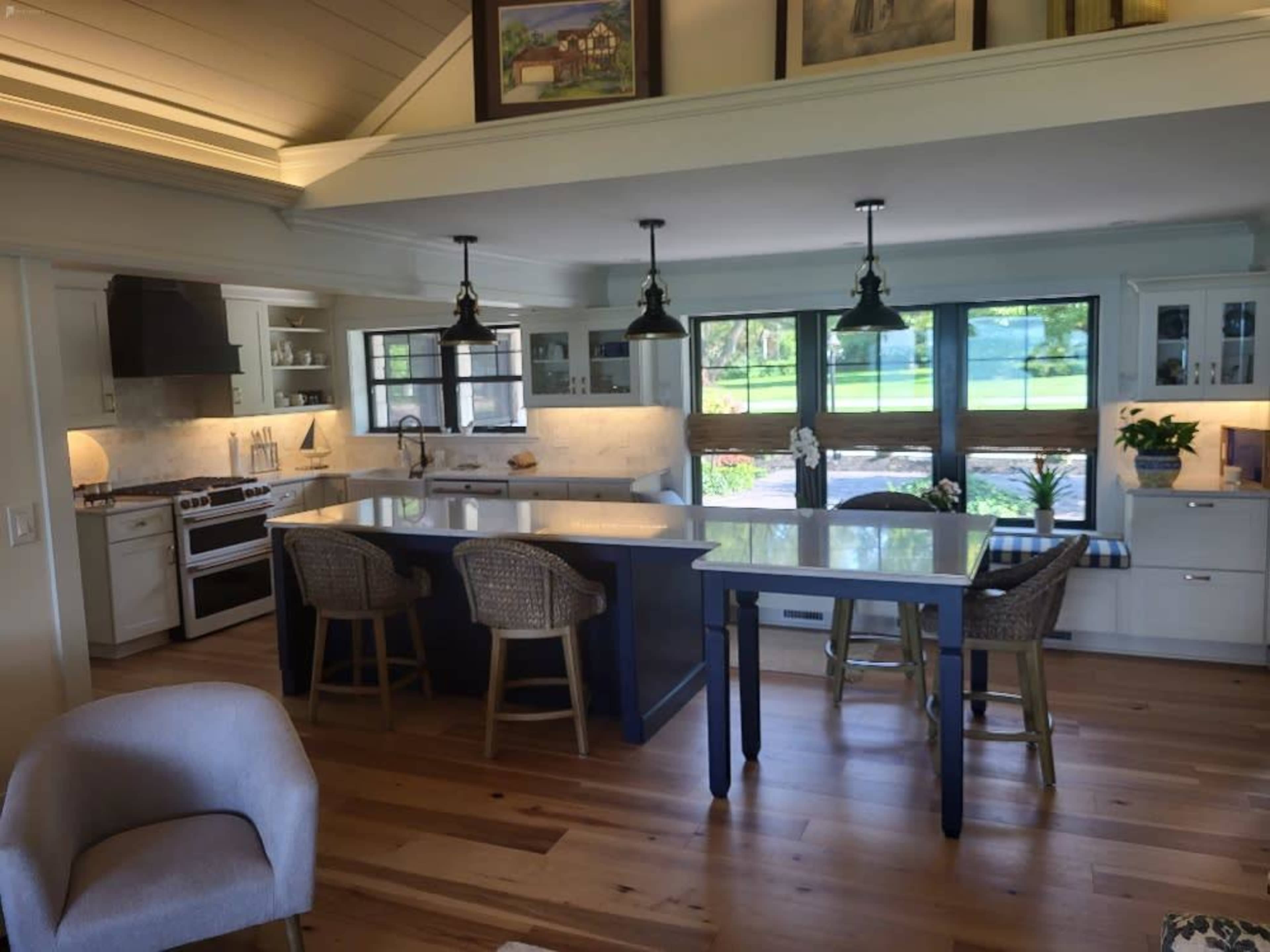A modern kitchen with an island, bar stools, and large windows overlooking a green landscape.