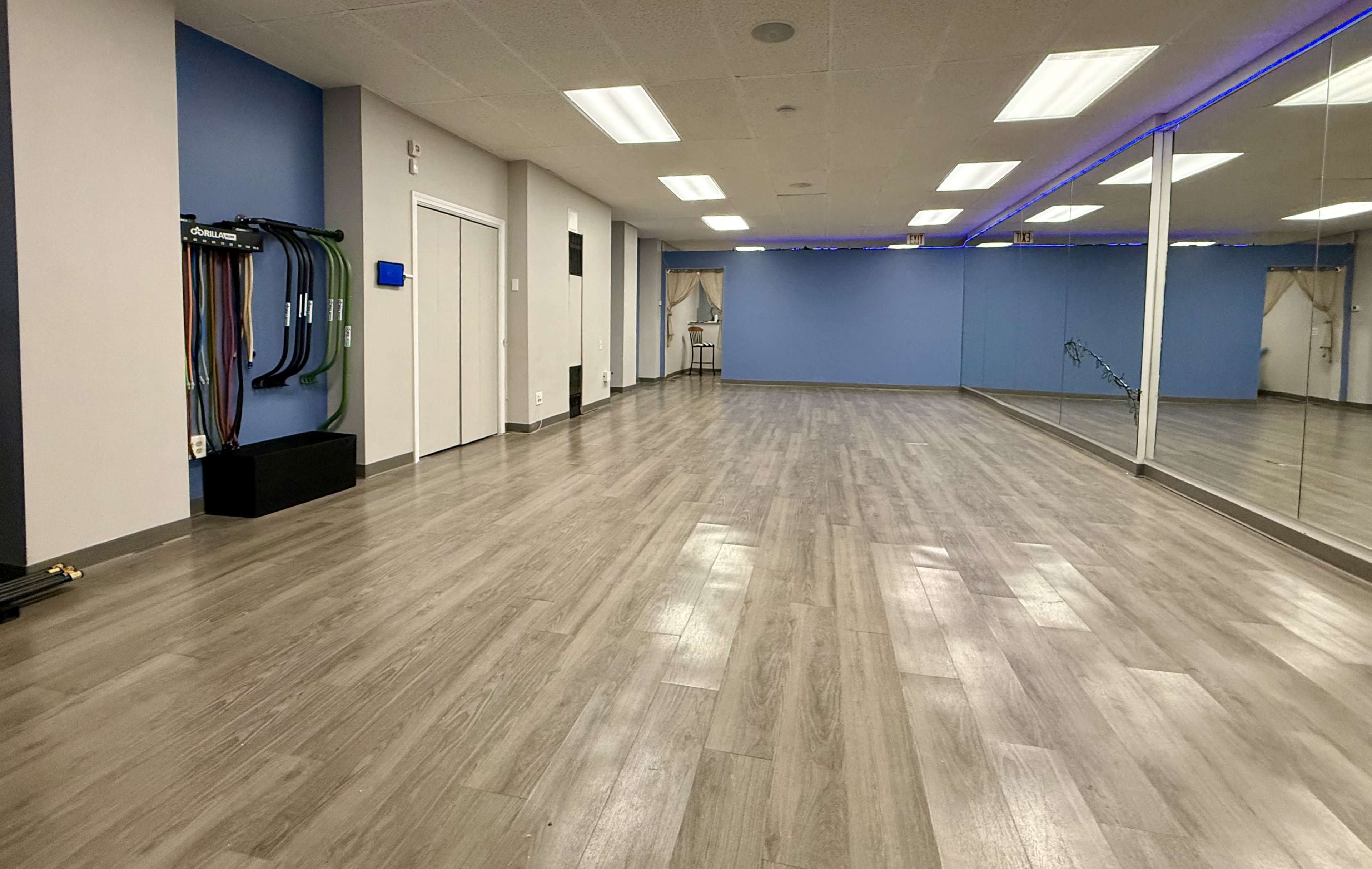 The image shows an empty interior of a fitness studio with gray wood flooring, blue walls, and mirrors along one side.
