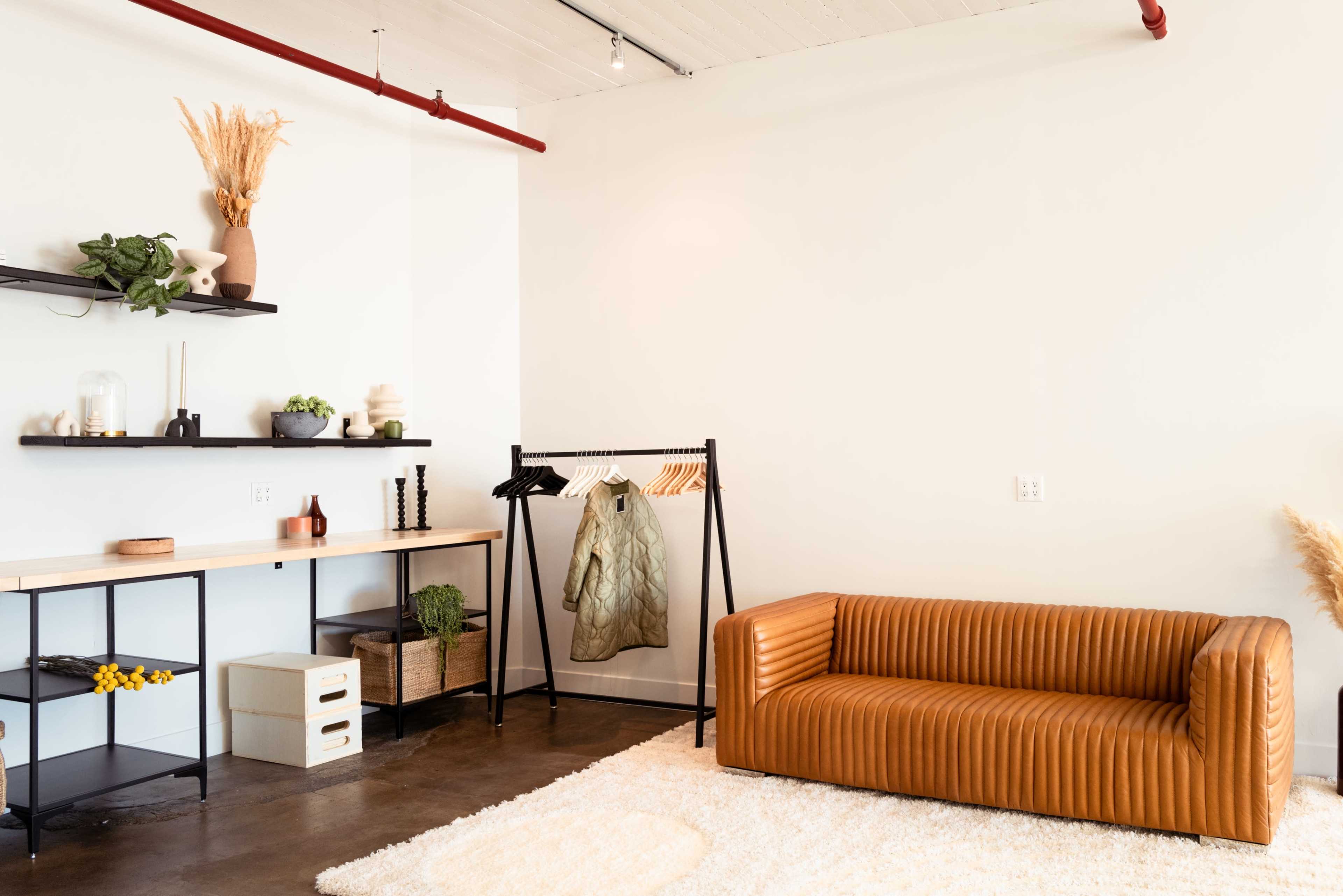 A minimalist interior with a brown ribbed sofa, a clothing rack, and a shelf containing decorative items and plants.