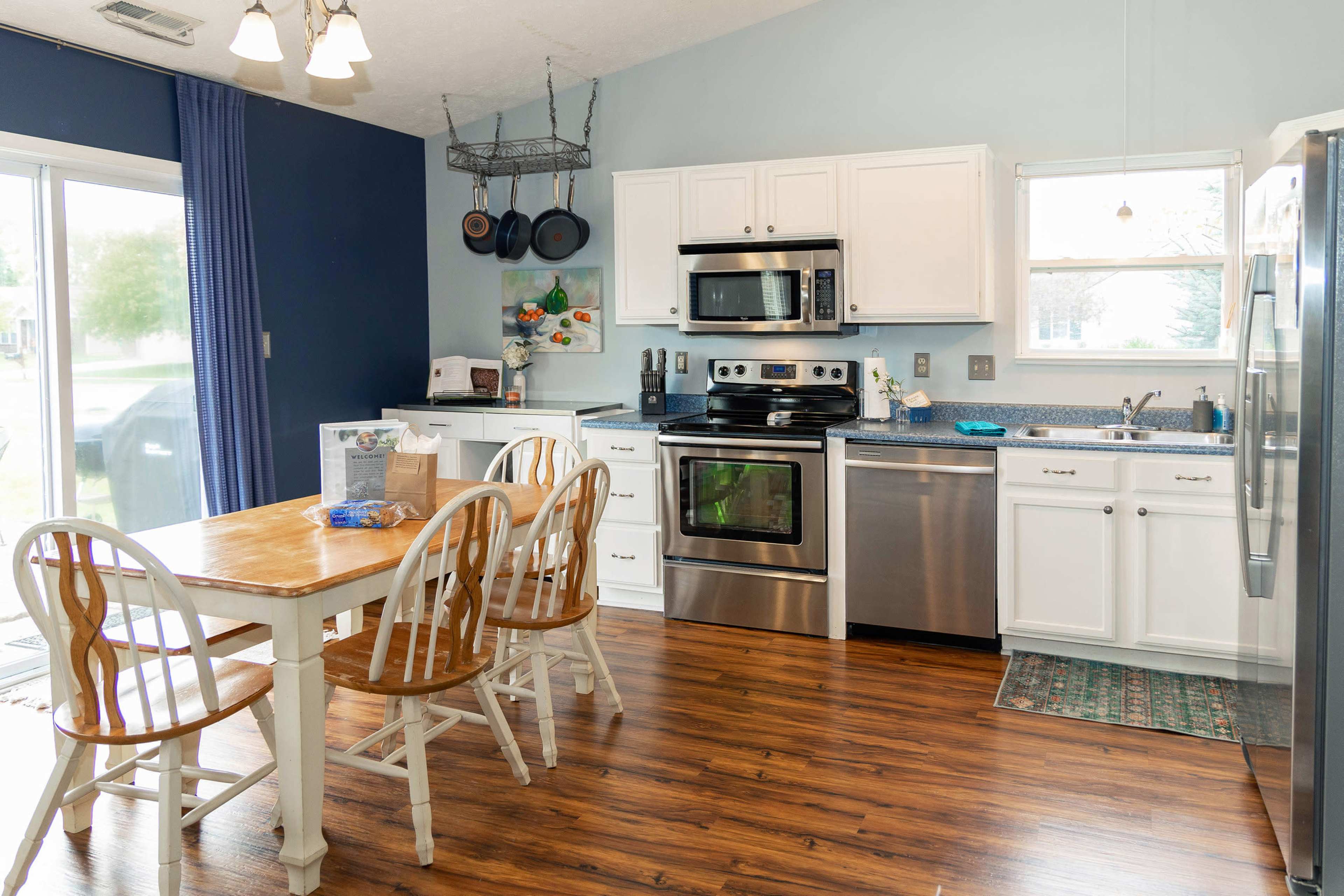 A kitchen with white cabinets, stainless steel appliances, a wooden dining table with white chairs, and blue walls.